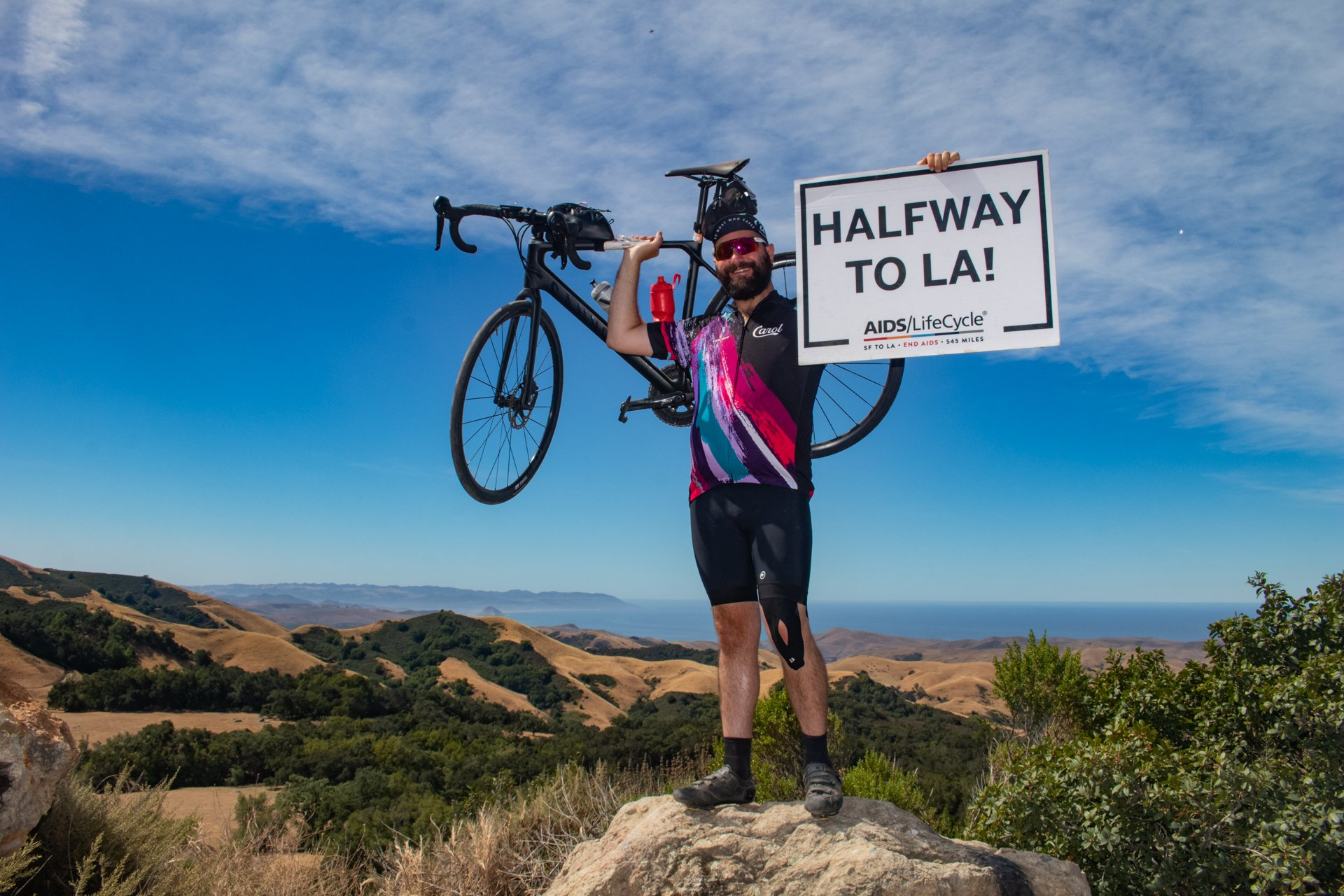 Izac standing with bike and sign that says half way to LA