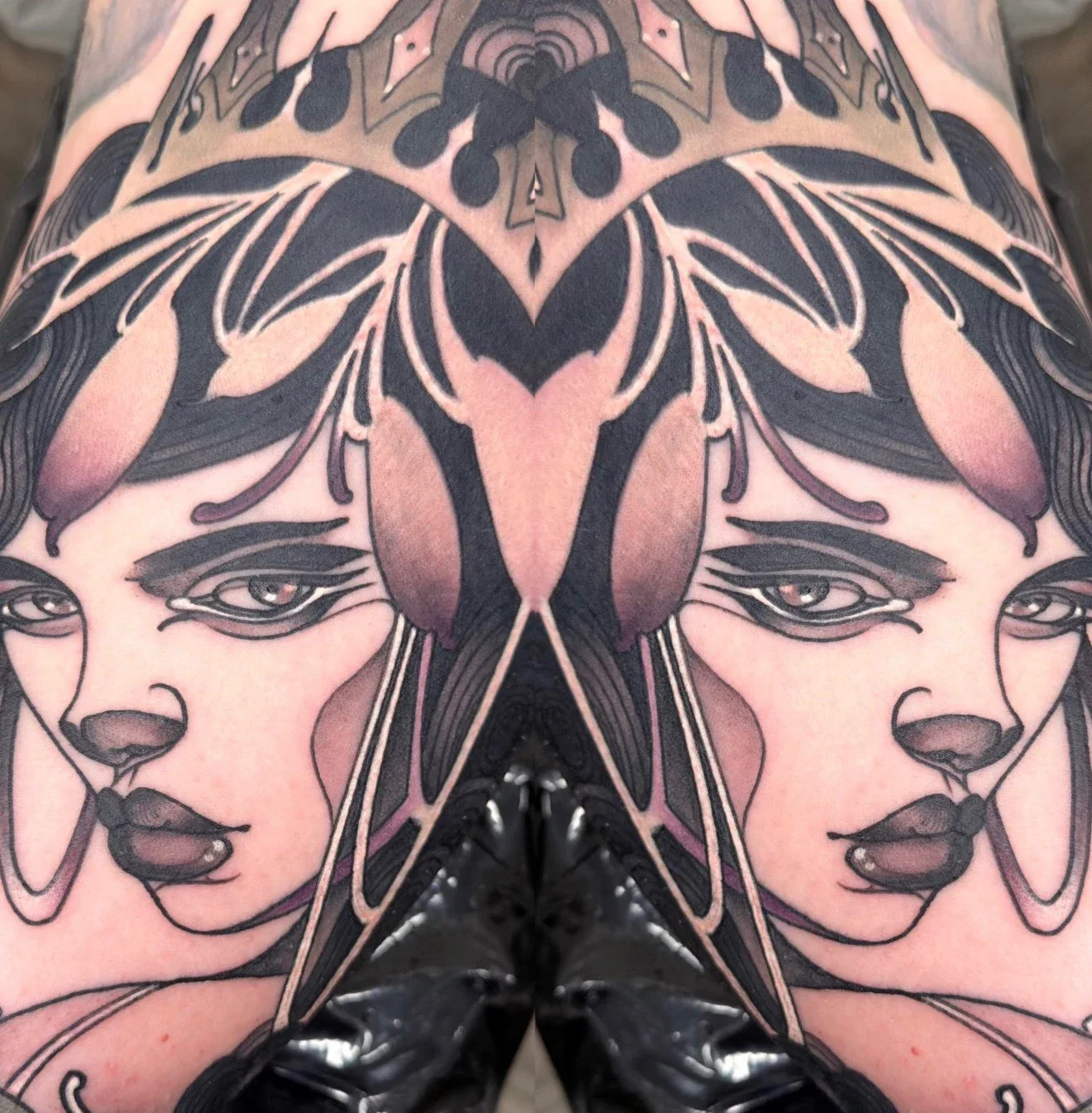 The Face, on Skin — Gia Rose's original flash design worn as a tattoo: a crowned lady's face mirrored in bold black linework with dusky blush shading, photographed on skin
