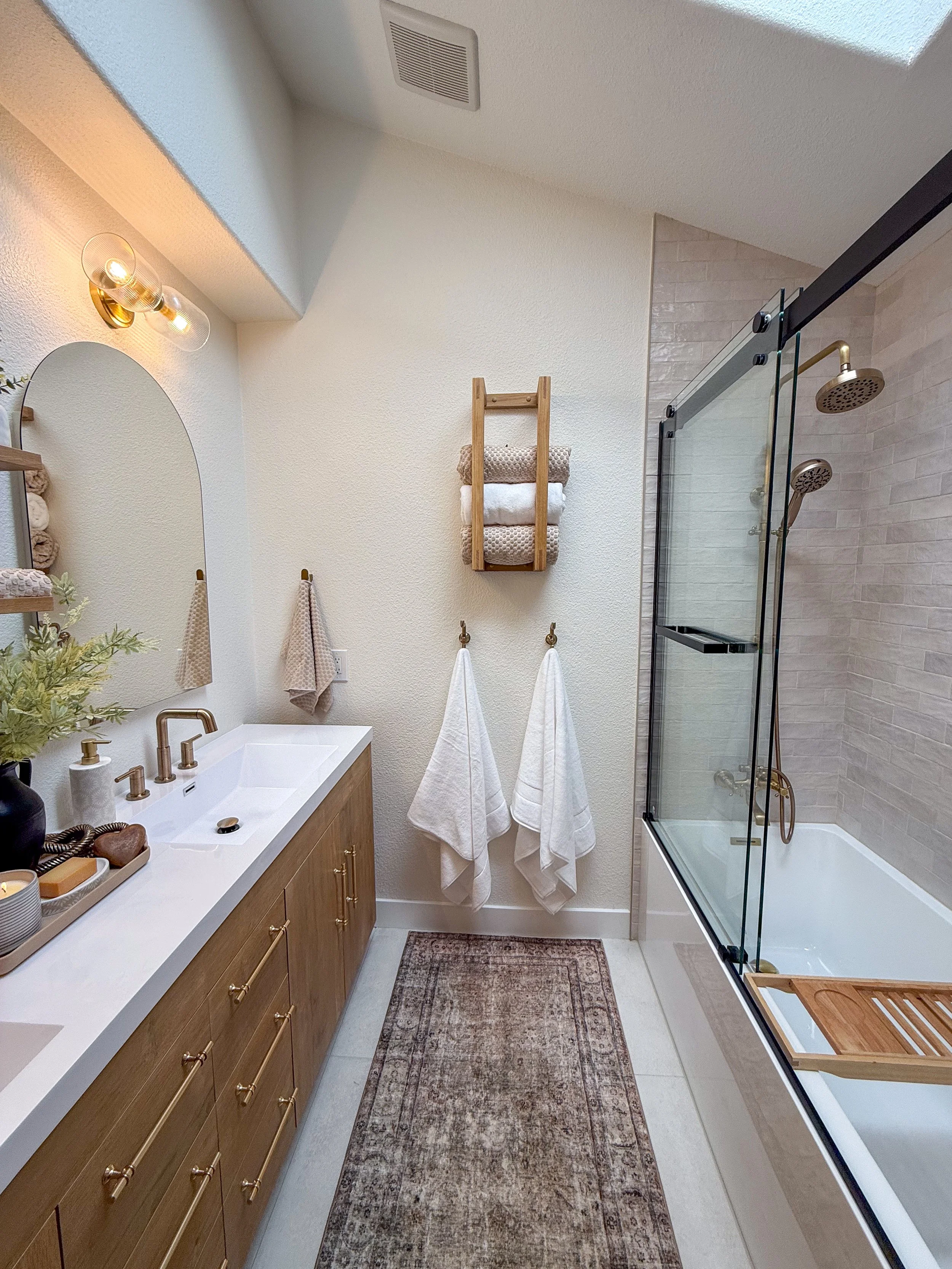 primary bathroom remodel, earthy bathroom inspiration, shower and bathtub combo, shower system with handheld sprayer, double vanity, wood vanity, floating shelves, arched medicine cabinets, toilet paper niche, double light sconce, brass finishes