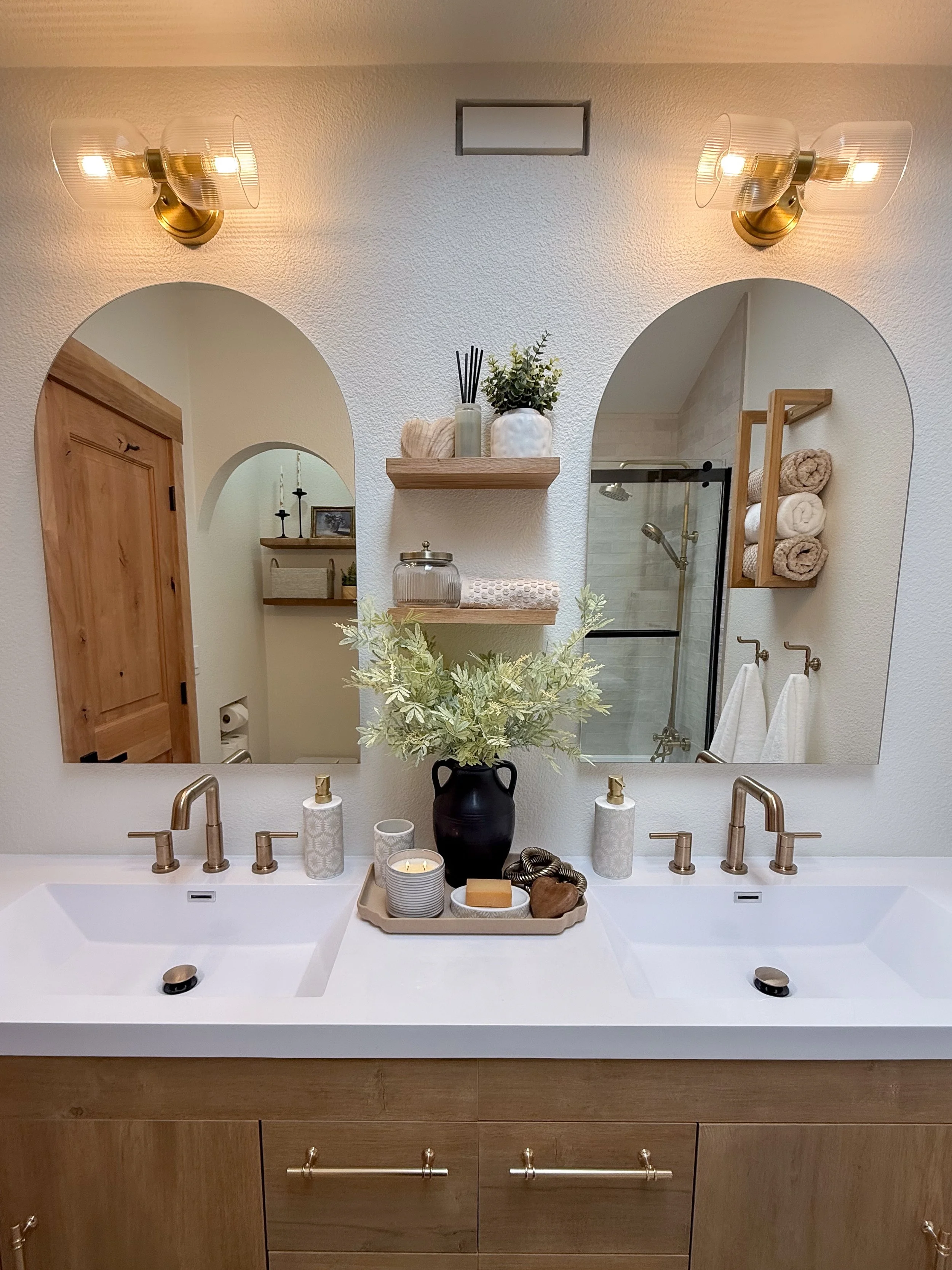 primary bathroom remodel, earthy bathroom inspiration, shower and bathtub combo, shower system with handheld sprayer, double vanity, wood vanity, floating shelves, arched medicine cabinets, toilet paper niche, double light sconce, brass finishes