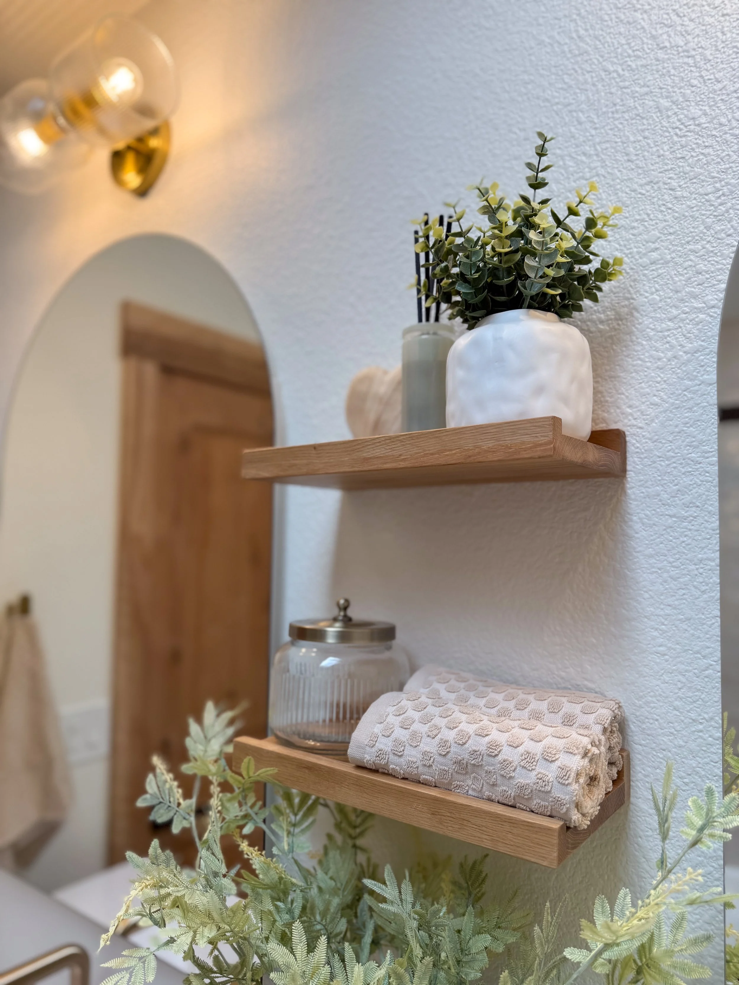 primary bathroom remodel, earthy bathroom inspiration, shower and bathtub combo, shower system with handheld sprayer, double vanity, wood vanity, floating shelves, arched medicine cabinets, toilet paper niche, double light sconce, brass finishes