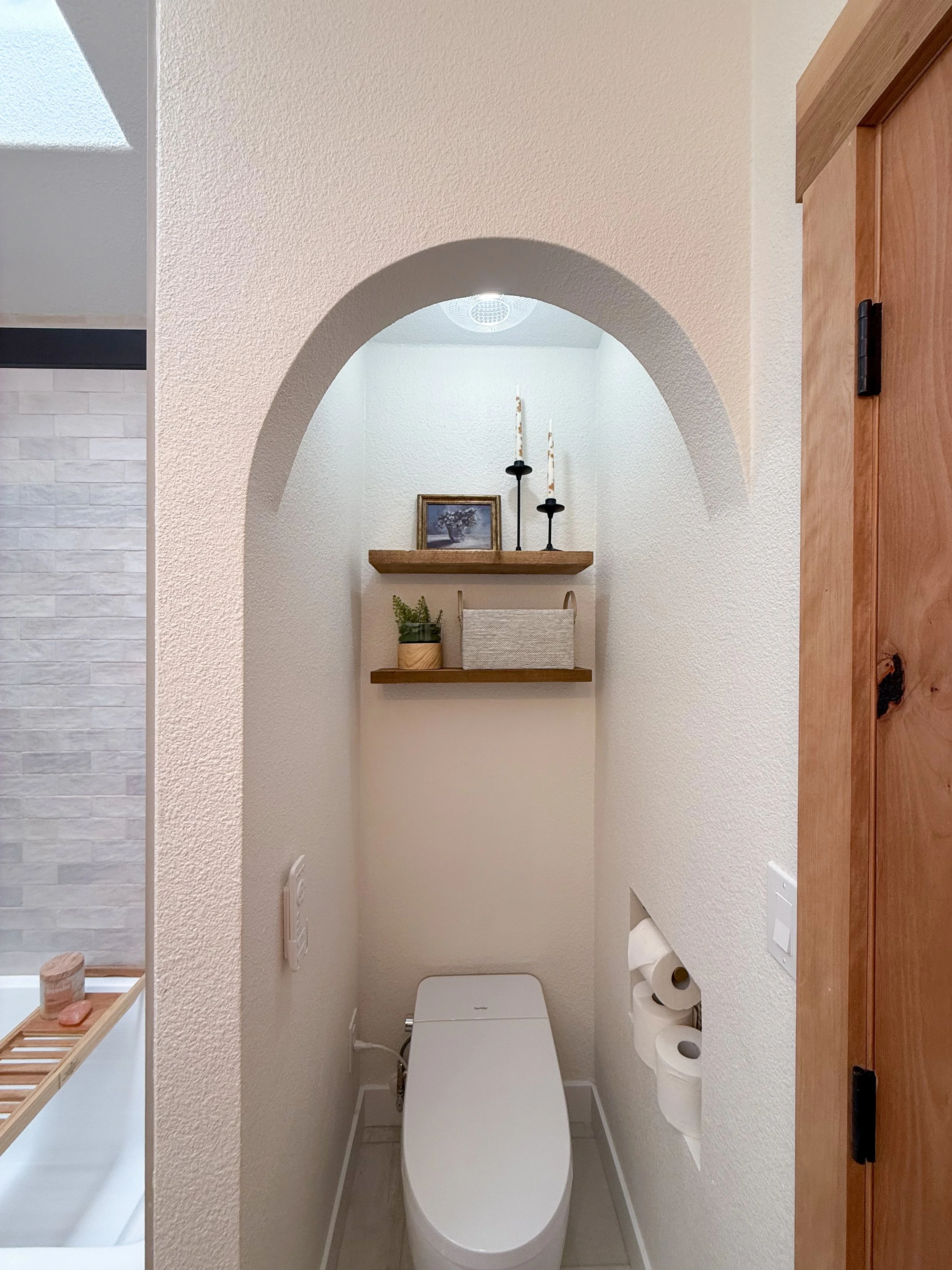 primary bathroom remodel, earthy bathroom inspiration, shower and bathtub combo, shower system with handheld sprayer, double vanity, wood vanity, floating shelves, arched medicine cabinets, toilet paper niche, double light sconce, brass finishes