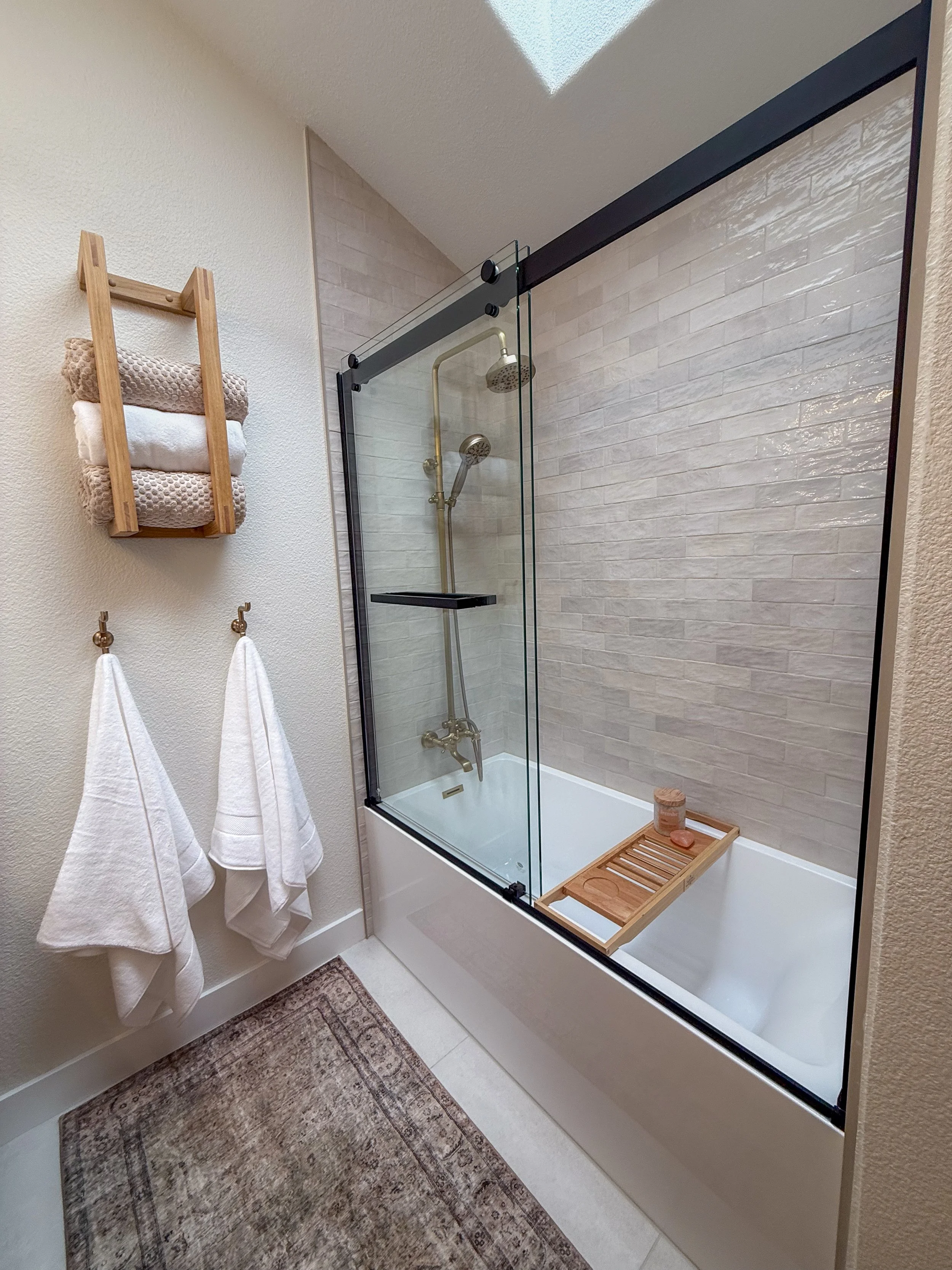 primary bathroom remodel, earthy bathroom inspiration, shower and bathtub combo, shower system with handheld sprayer, double vanity, wood vanity, floating shelves, arched medicine cabinets, toilet paper niche, double light sconce, brass finishes