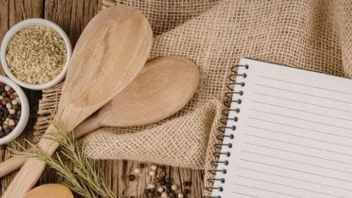 Recipe book, wooden spoons and some spices on a table.