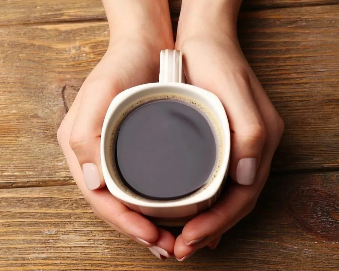 Woman's hands cupping a mug of coffee on a wooden table.