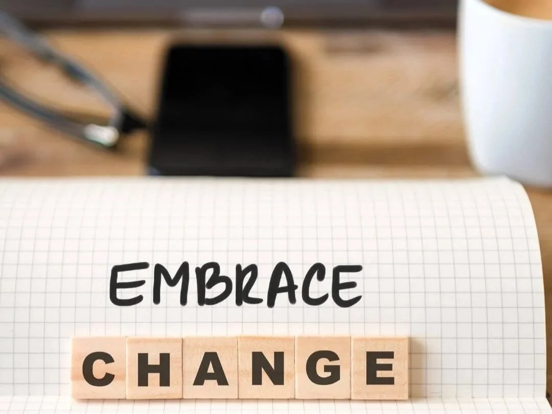 Grid note pad with the word embrace written on it and scrabble tiles spelling out change.