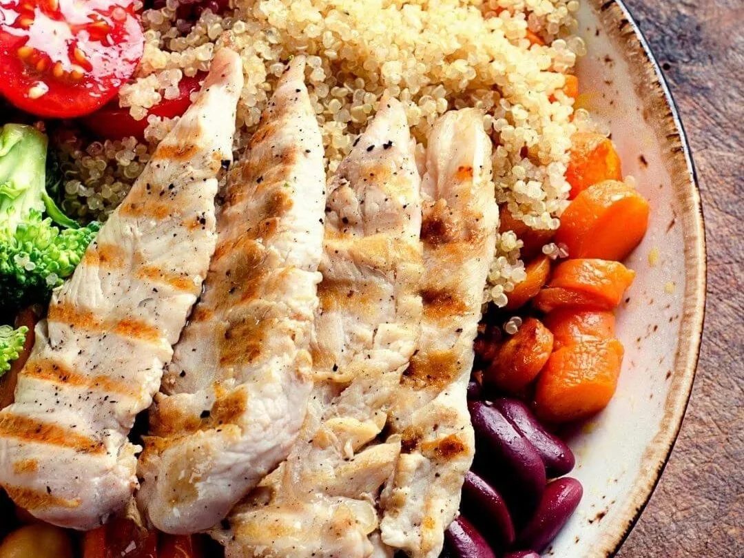 Plate of healthy food including chicken breast, carrots, broccoli and quinoa.