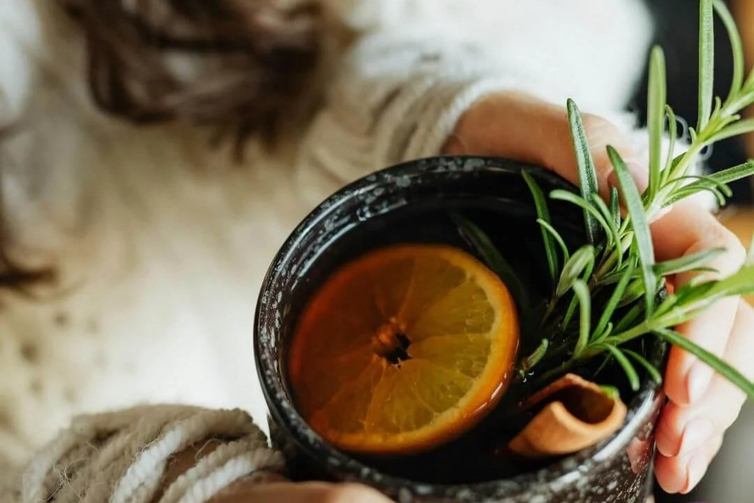 Wpman in white sweater holding a warm black mug of liver detox tea made with orange, rosemary and cinnamon.
