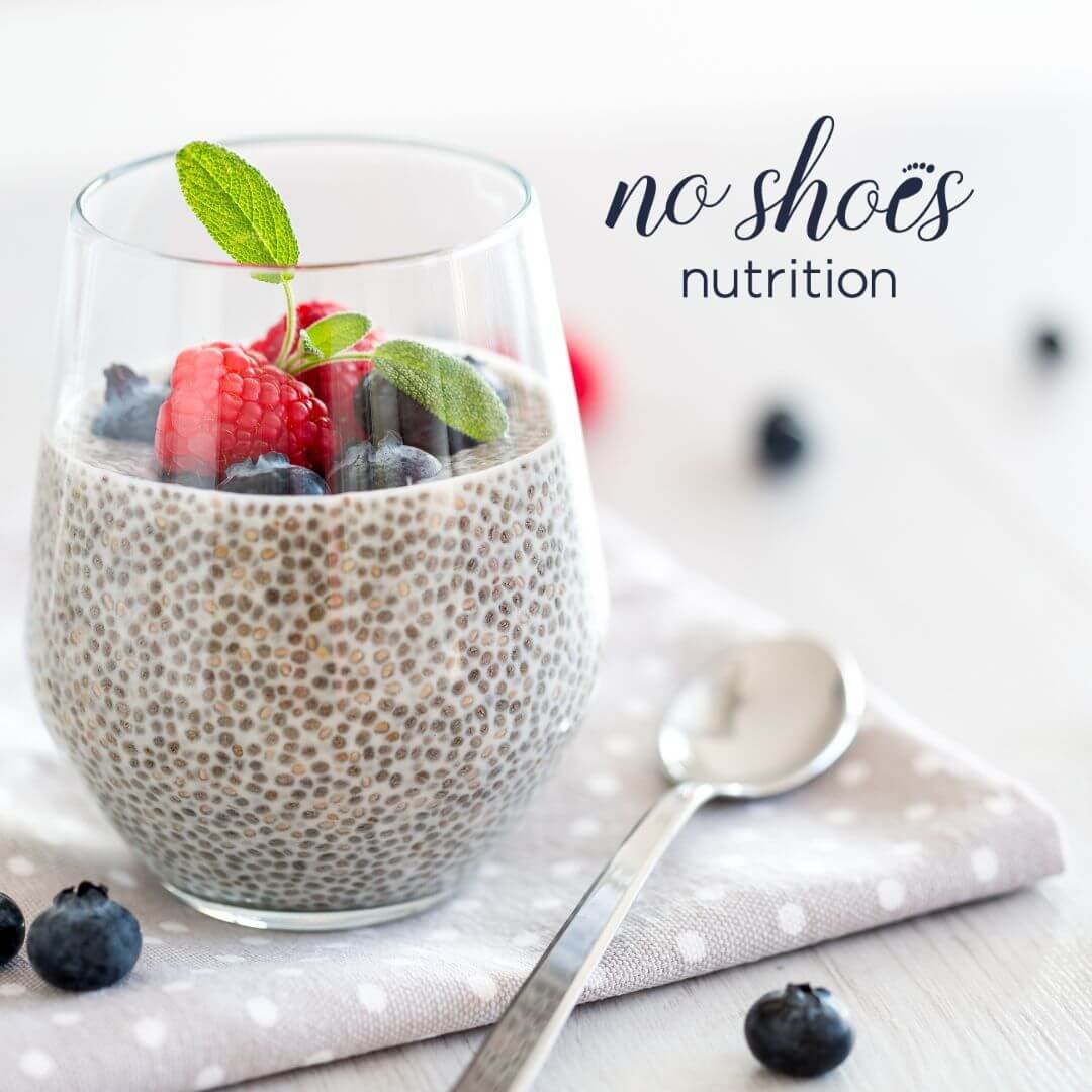 A wine glass filled with chia pudding and berries with a spoon and napkin on a table.