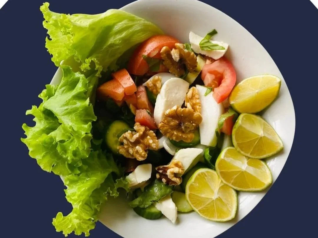 Bowl of salad with balanced protein, fat and fibre. White bowl with greens, tomato, walnuts and cucumber.