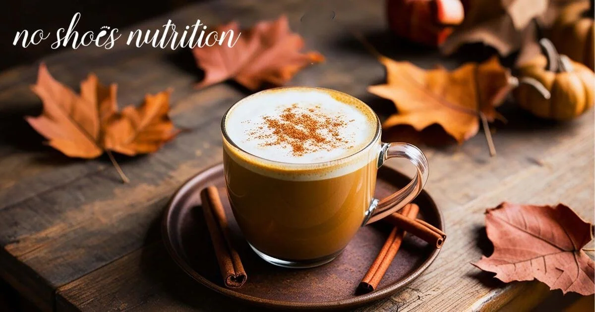 A warm drink in a glass mug on a wood table with orange fall maple leaves around it.