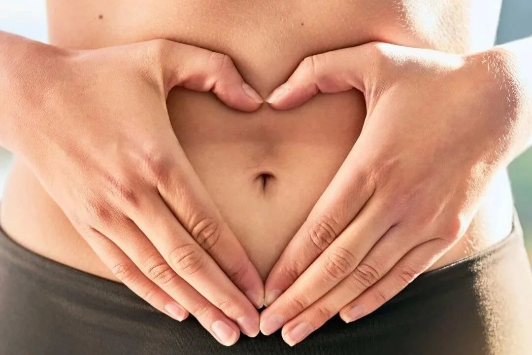 Women with exposed midsection making a heart with her hands over her belly.
