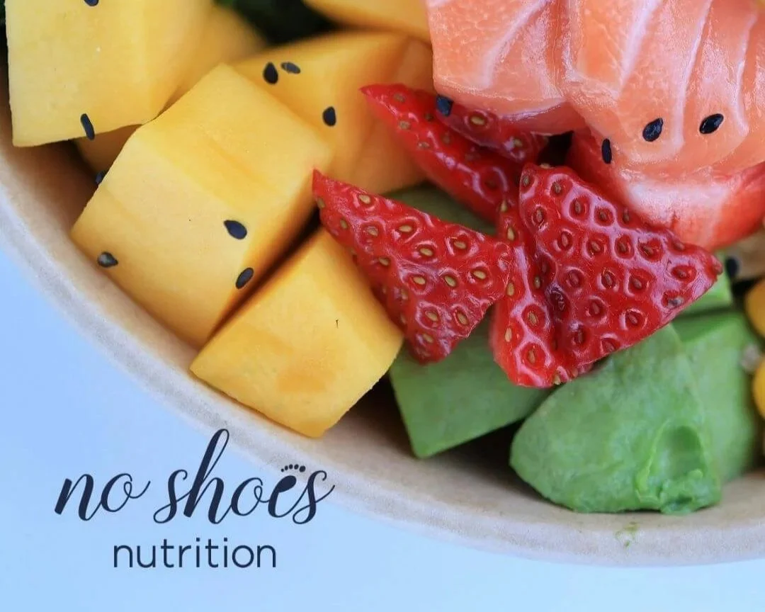 Bowl of brain healthy foods like fruit and salmon on a blue background.