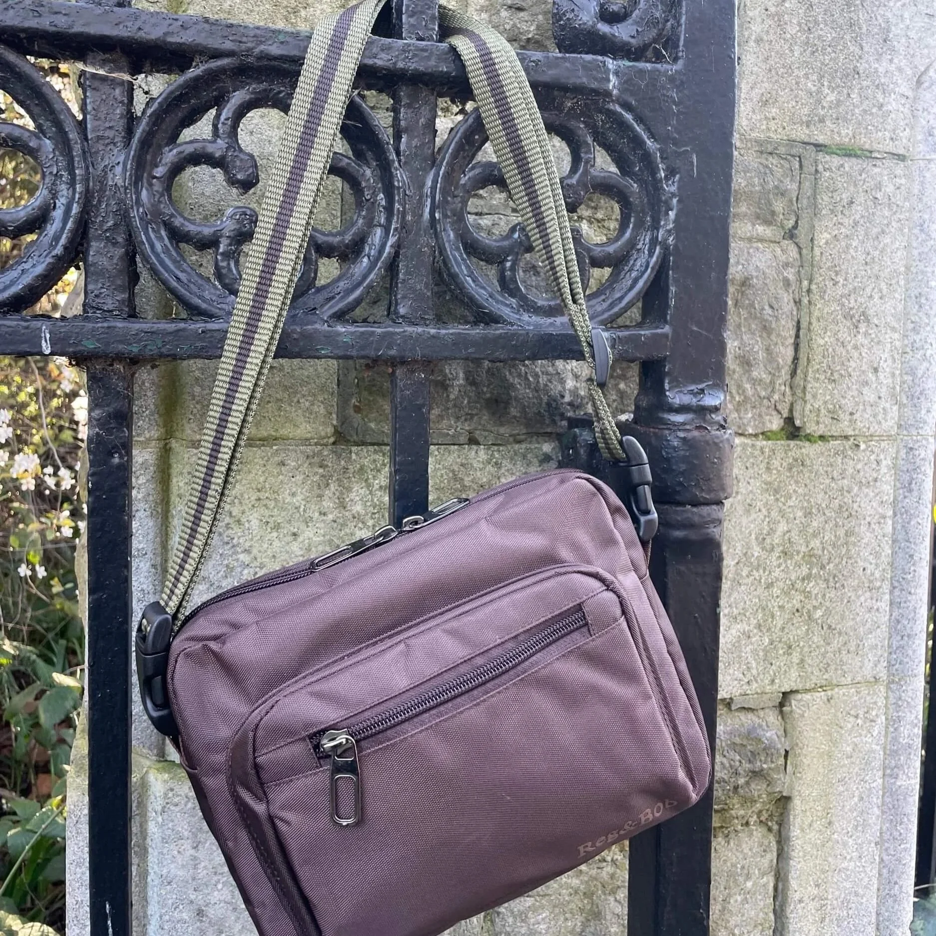 brown Reg&Bob dog walking bag with khaki strap hanging on black railings