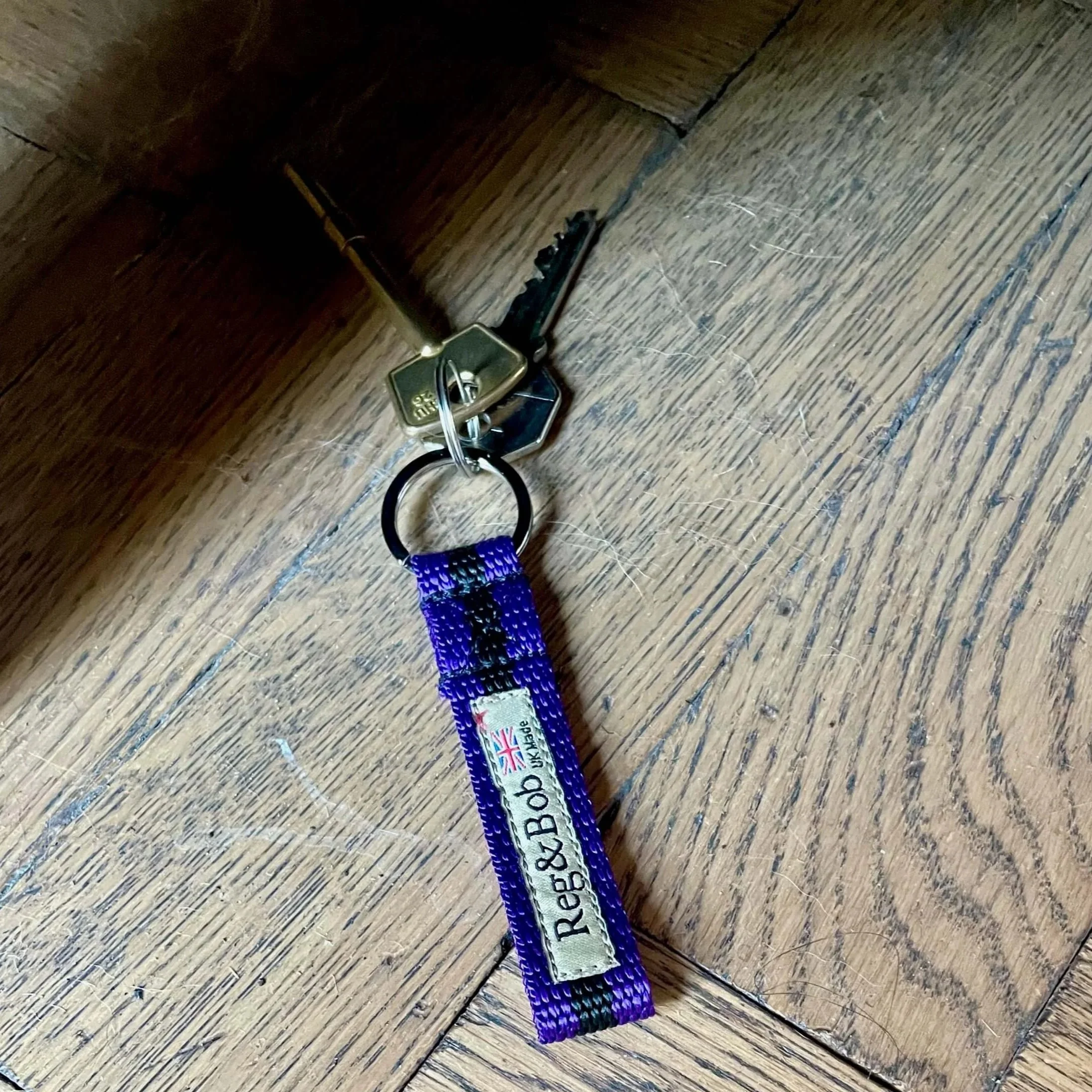keys on a blue striped Reg&Bob keyring sitting on a wood floor