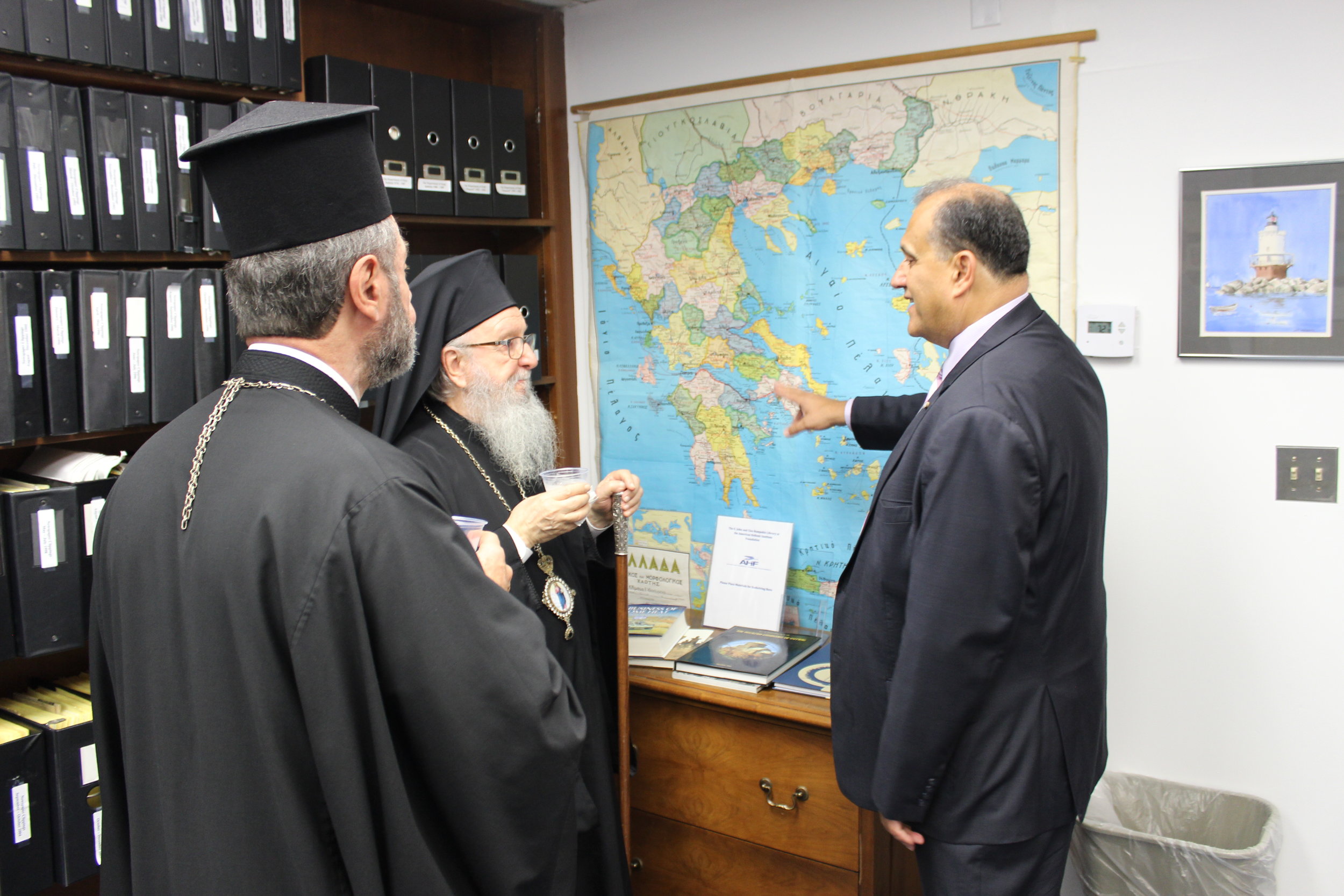  His Eminence Archbishop Demetrios of America, AHI President Nick Larigakis, and Bishop Sevastianos of Zela discussing the heritage of their families in front of a map of Greece. 
