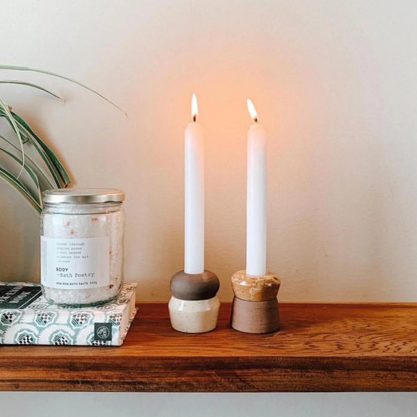 Sundays. 

Image description: A jar of bath salts sits on a book beside two ceramic candle holders with lit tapered white candles on a wooden shelf. The image is warm and inviting, with glowing cozy candle light. Some greenery peaks into the left sid