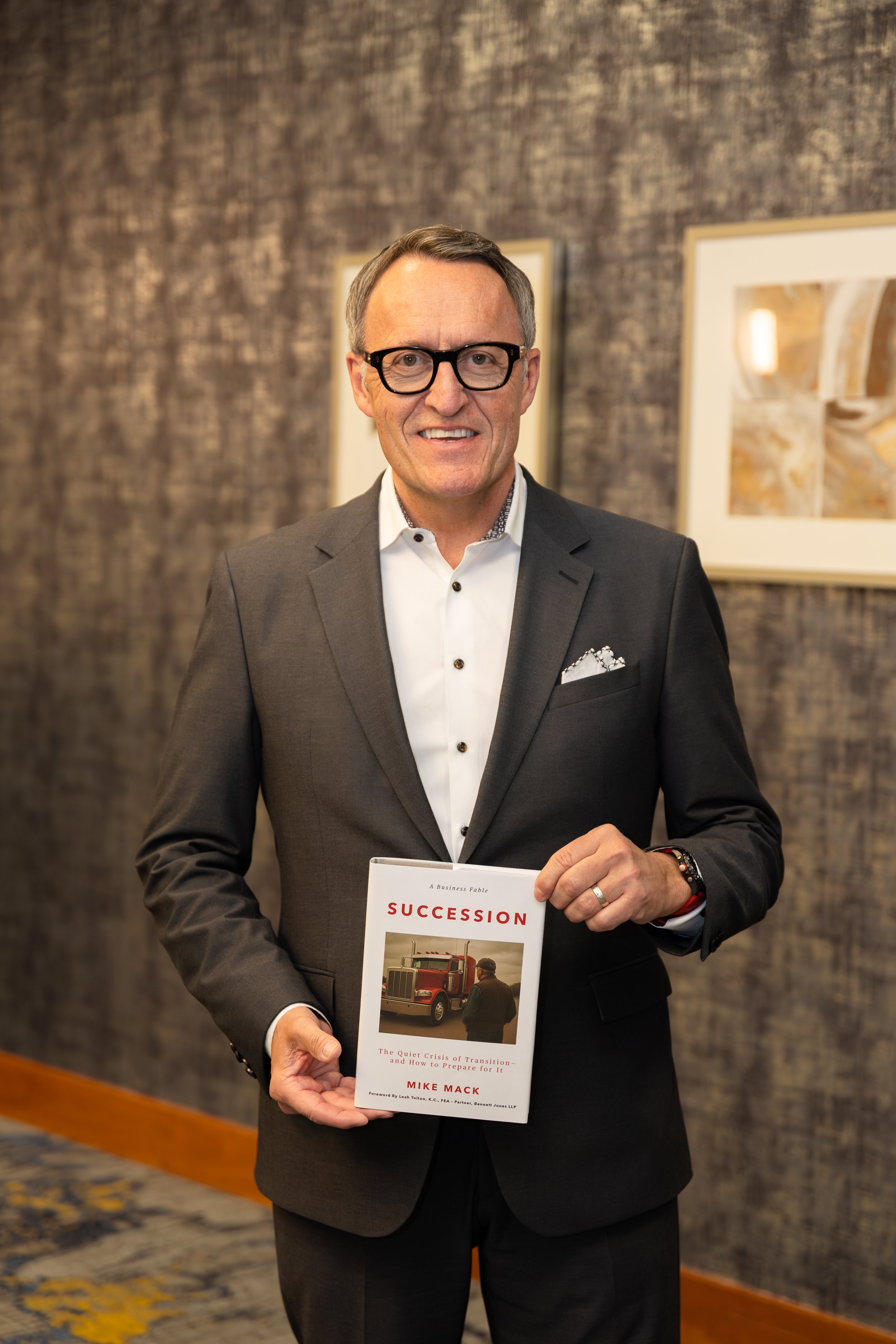 Mike Mack standing holding his book on Succession