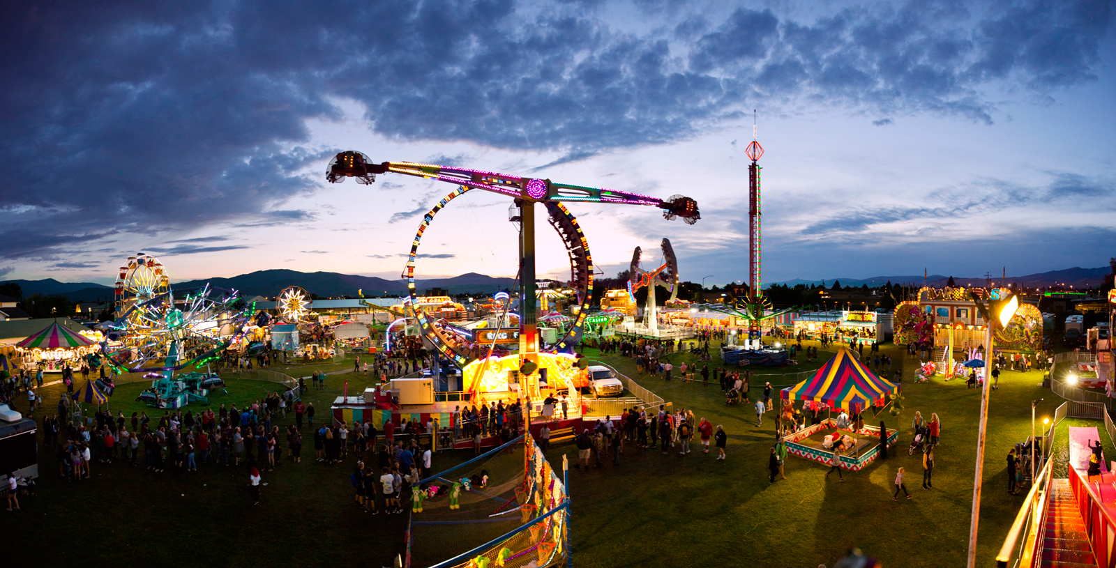Photo by Bess Bird. Rides glow at dusk as long lines gather.
