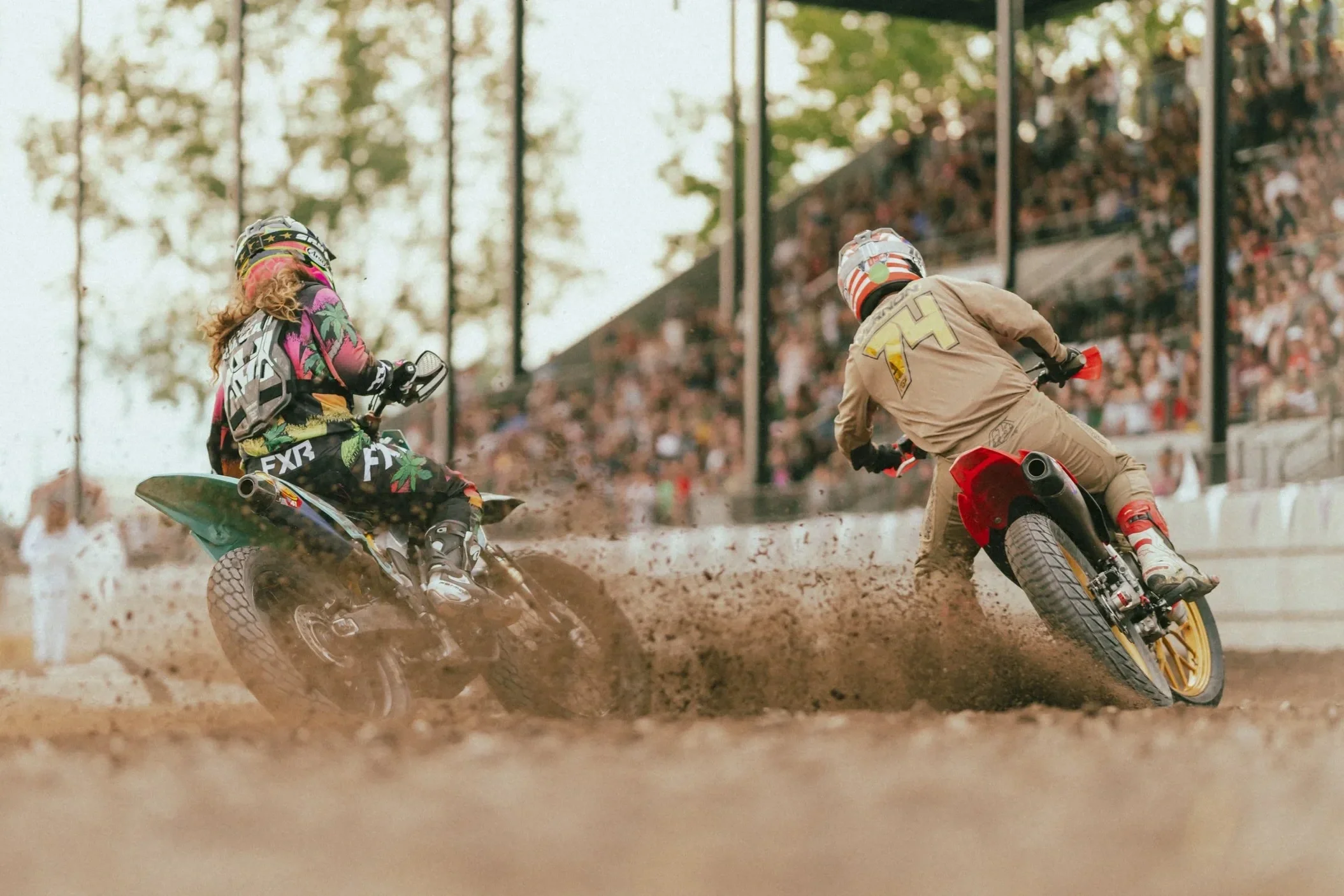 Two motocross riders racing on a dirt track, with a crowd of spectators in the Clouse Bauer Arena grandstands.