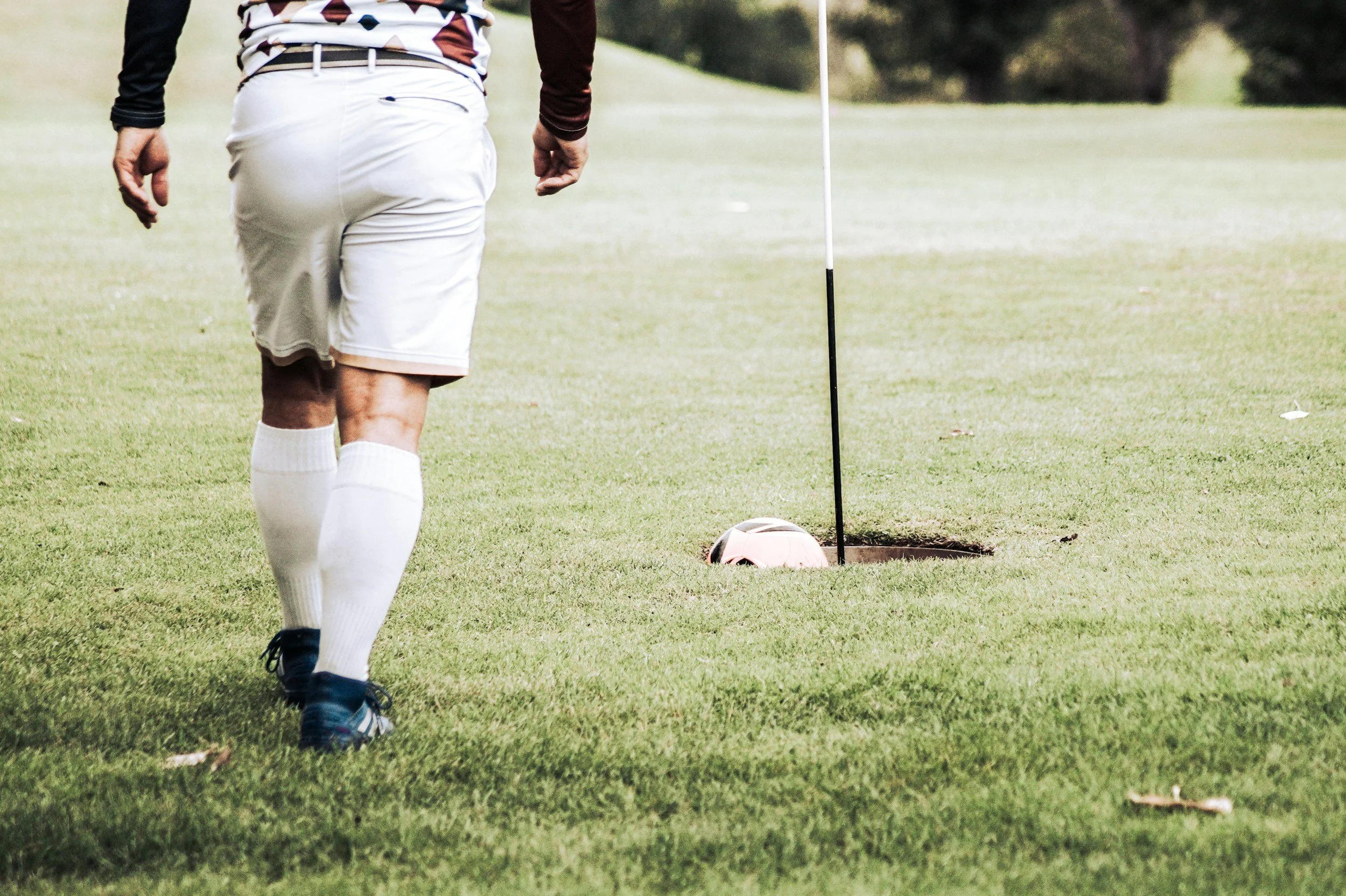Player shooting soccer ball into large golf hole.