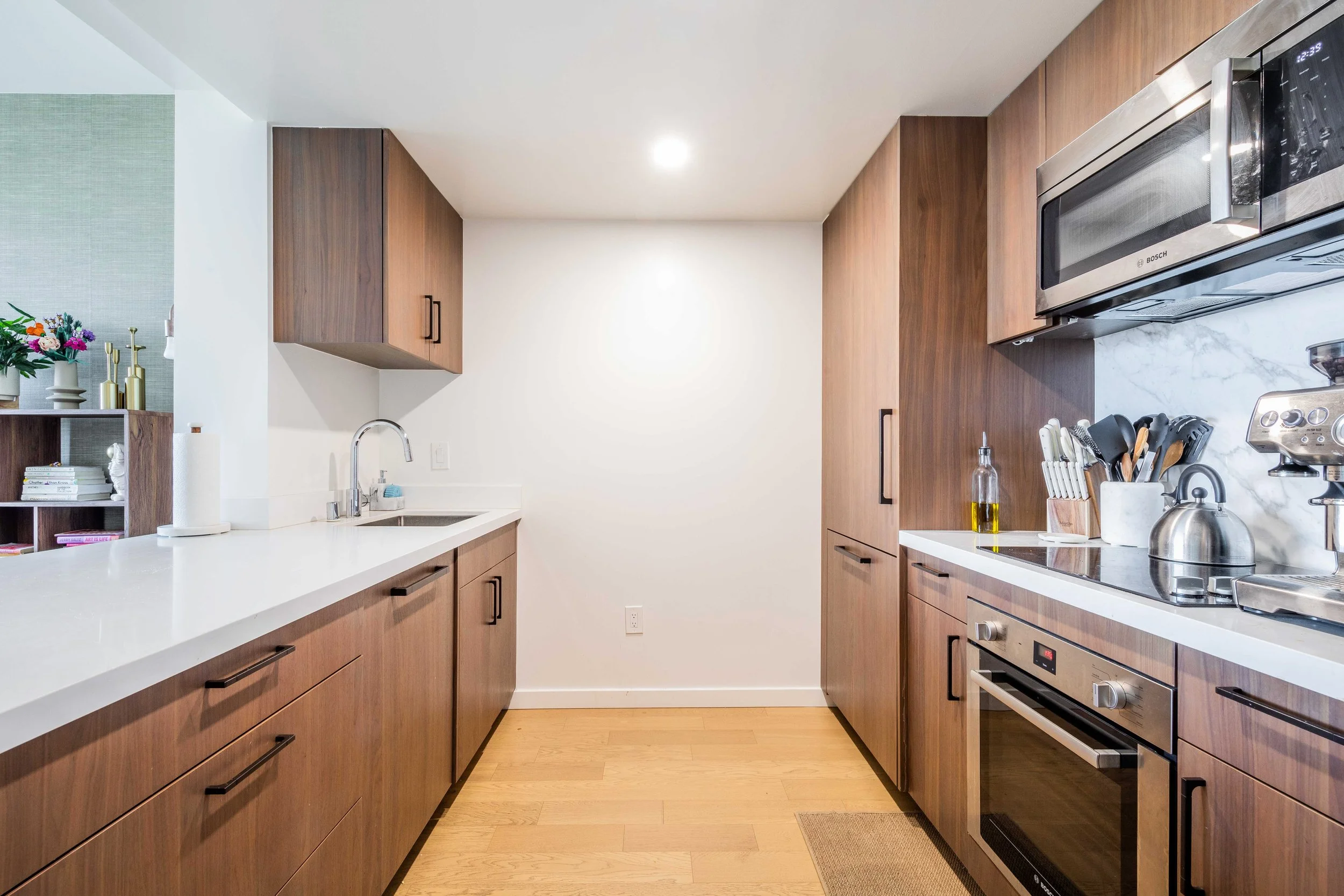 Modern kitchen with wooden cabinets, white countertops, stainless steel appliances, and a small rug on light wood flooring.