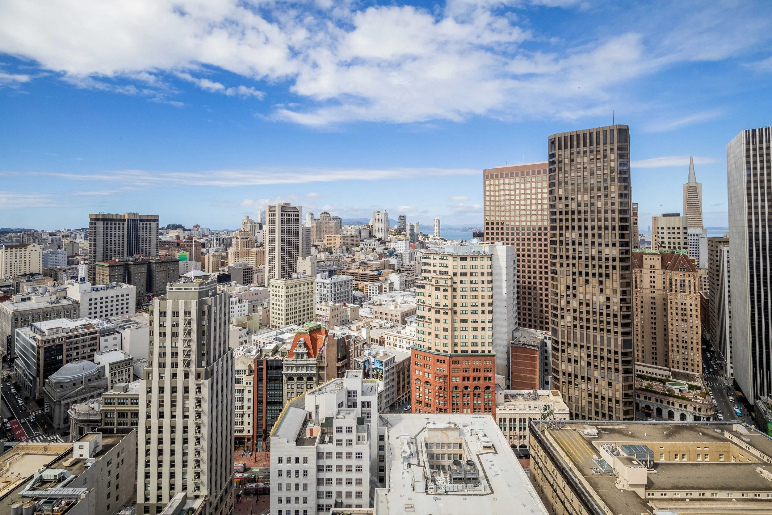 A panoramic view of a city skyline with tall buildings, including the Transamerica Pyramid, under a partly cloudy blue sky.
