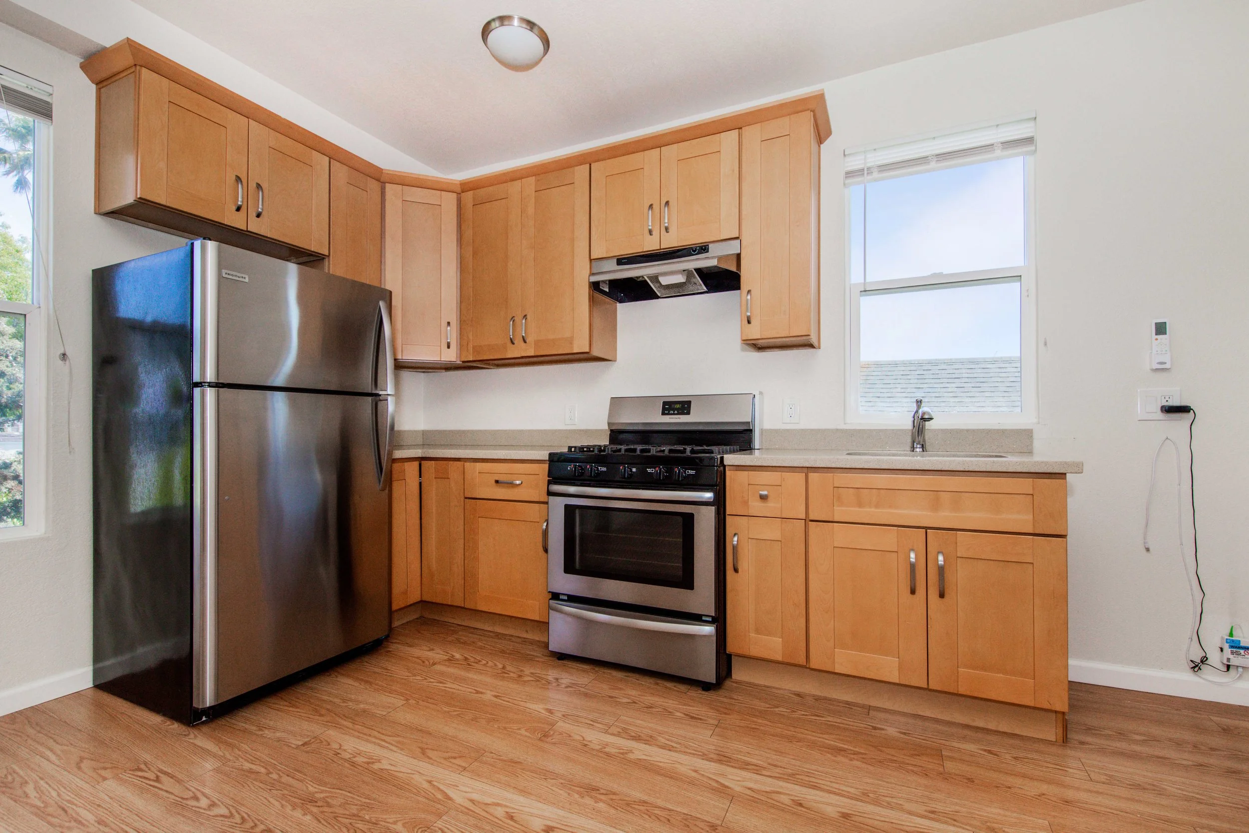 Kitchen with wooden cabinets, stainless steel refrigerator, stove, and a window above the sink.