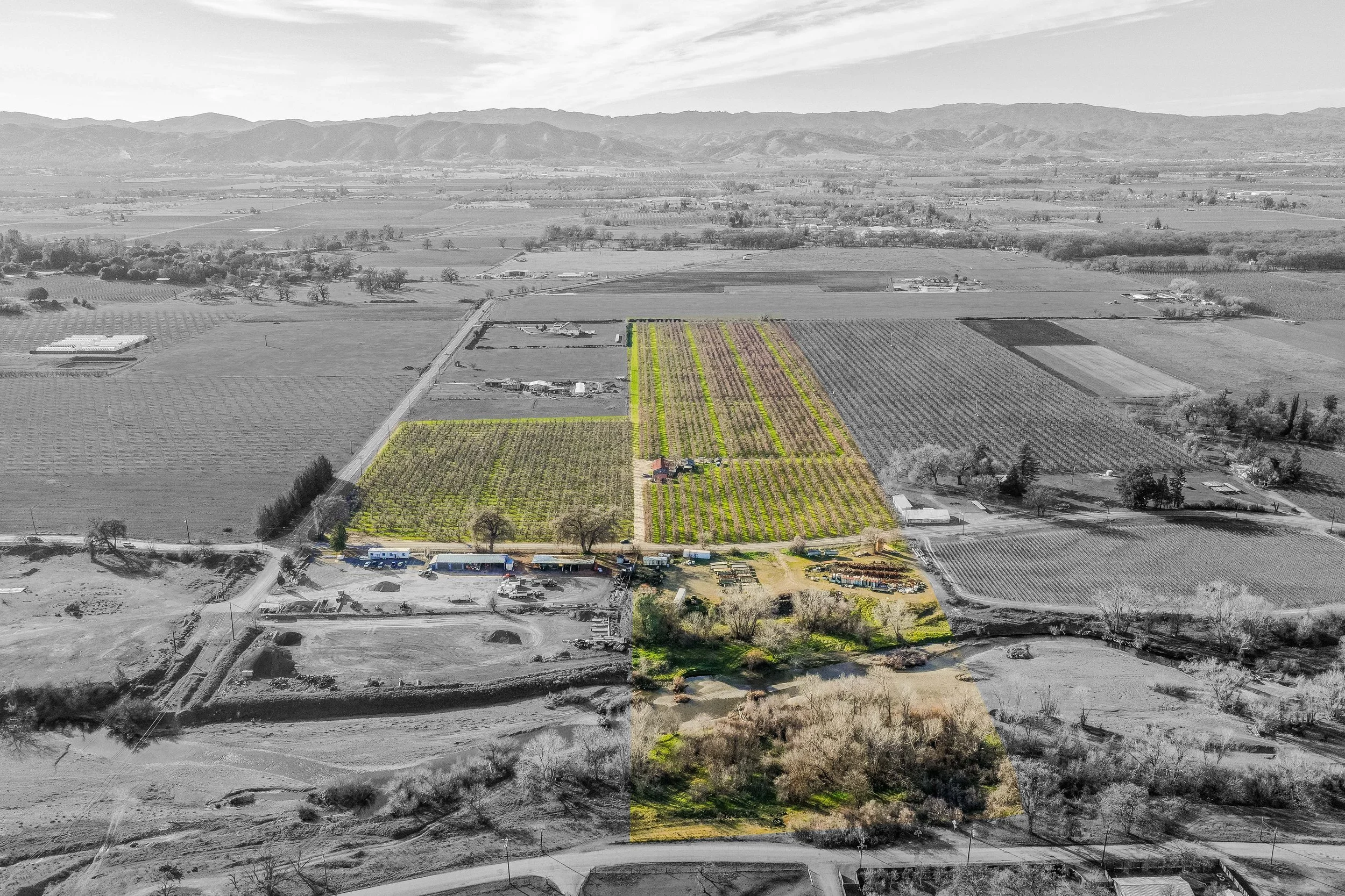 Aerial view of farmland with cultivated fields, a river, and a few buildings, some in color and some in black and white.