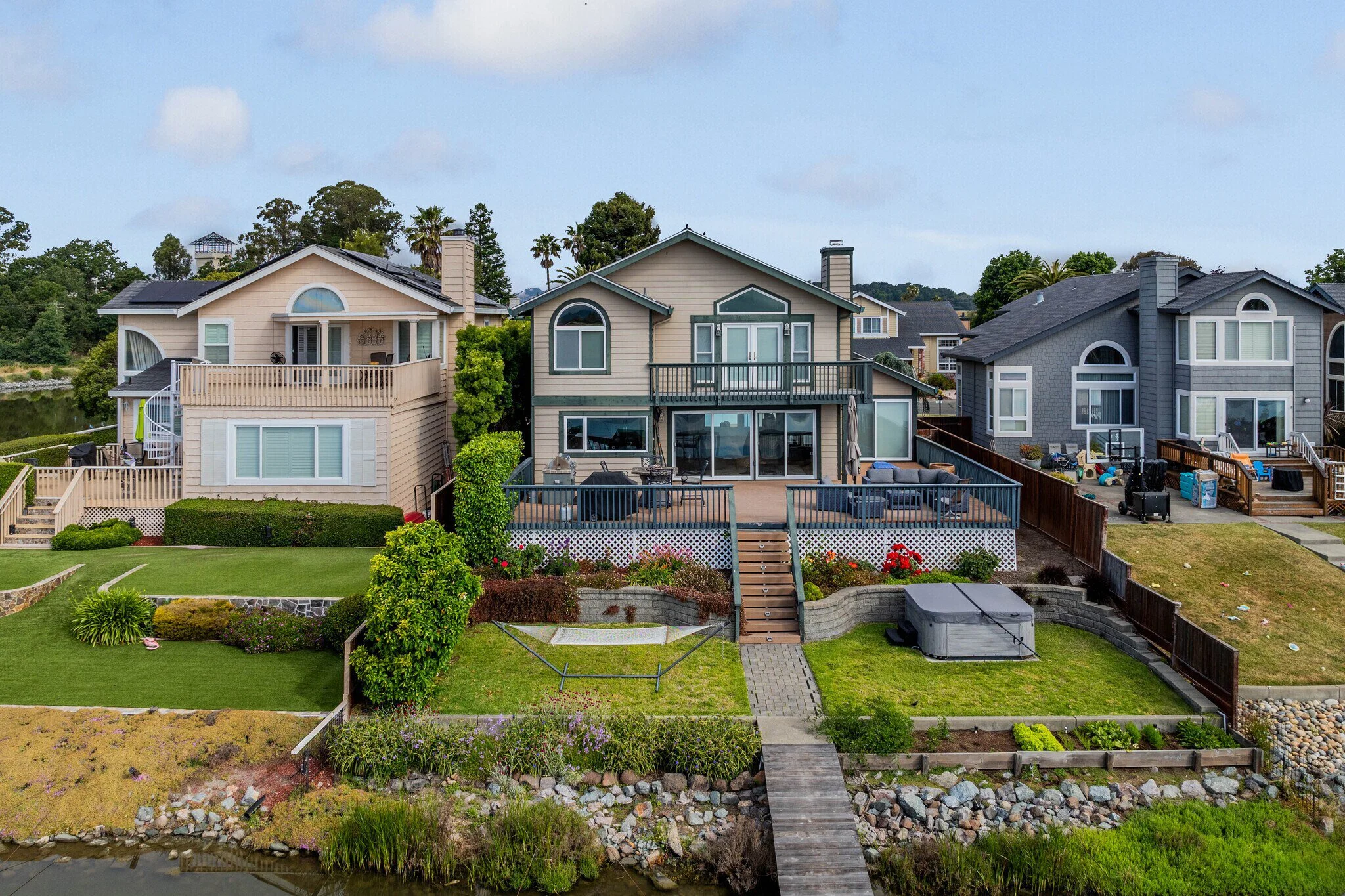 Multi-story houses on waterfront with grassy yards and wooden decks.