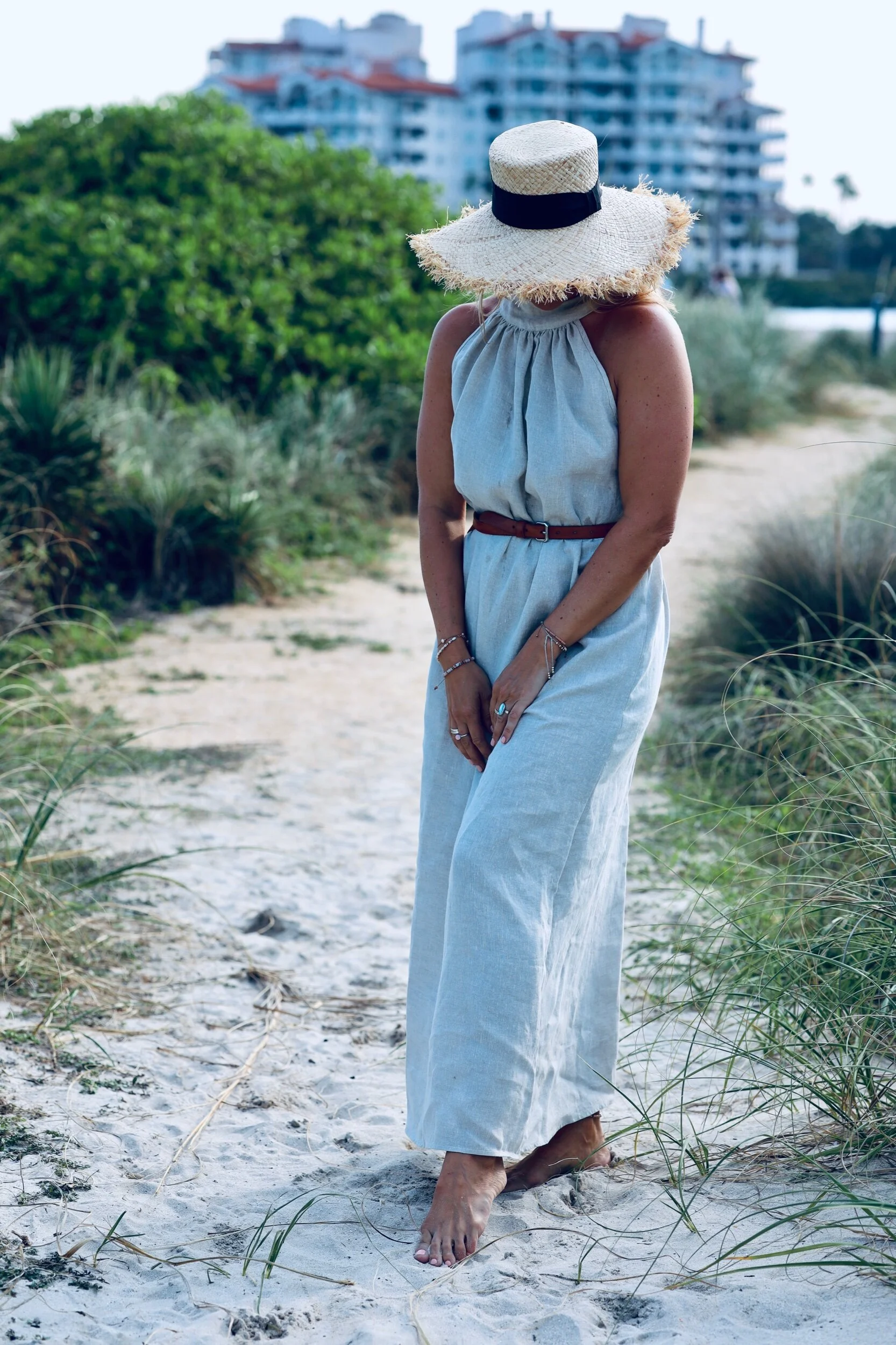 Woman wearing baby blue linen dress on sandy path.