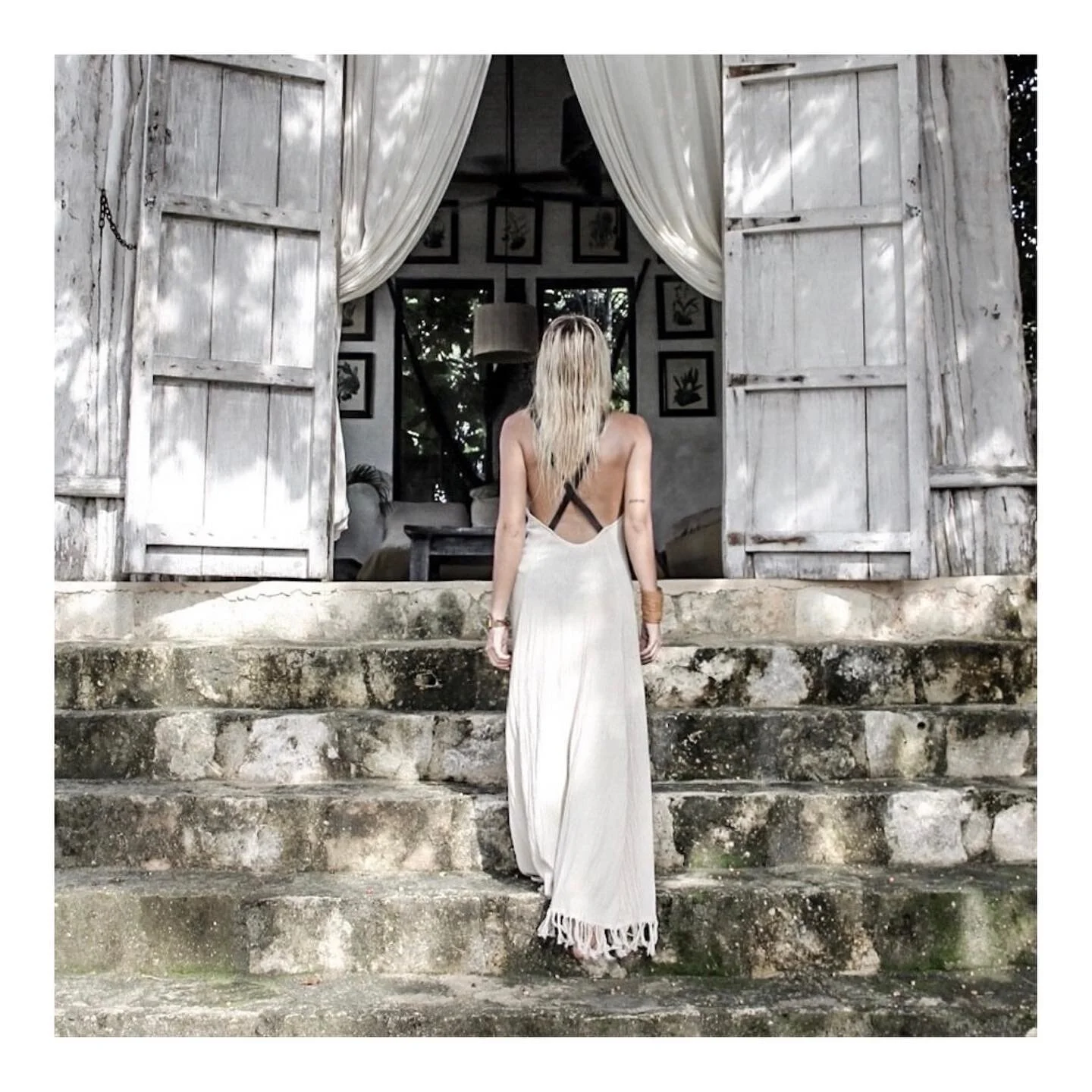 Woman wearing white dress in open doorway facing backwards.