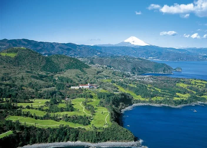 Paisaje de montañas verdes, un lago y volcán cubierto de nieve al fondo bajo cielo azul.