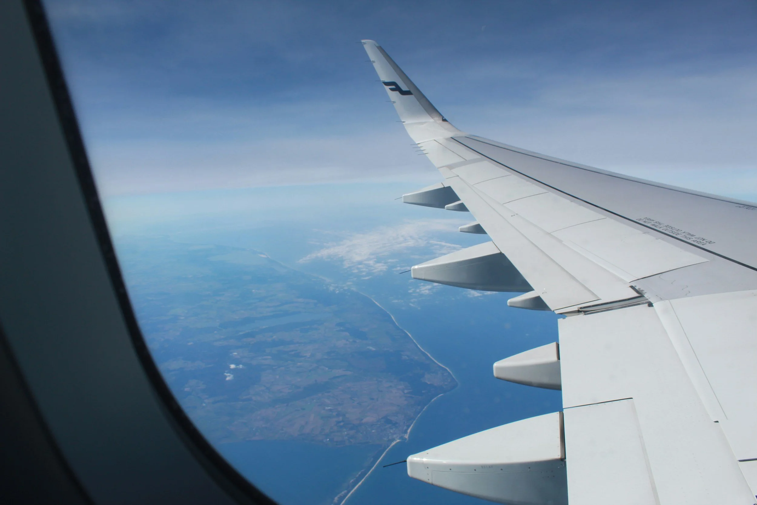 Vista desde la ventana del avión mostrando la ala del avión y el paisaje terrestre con agua y tierra debajo.