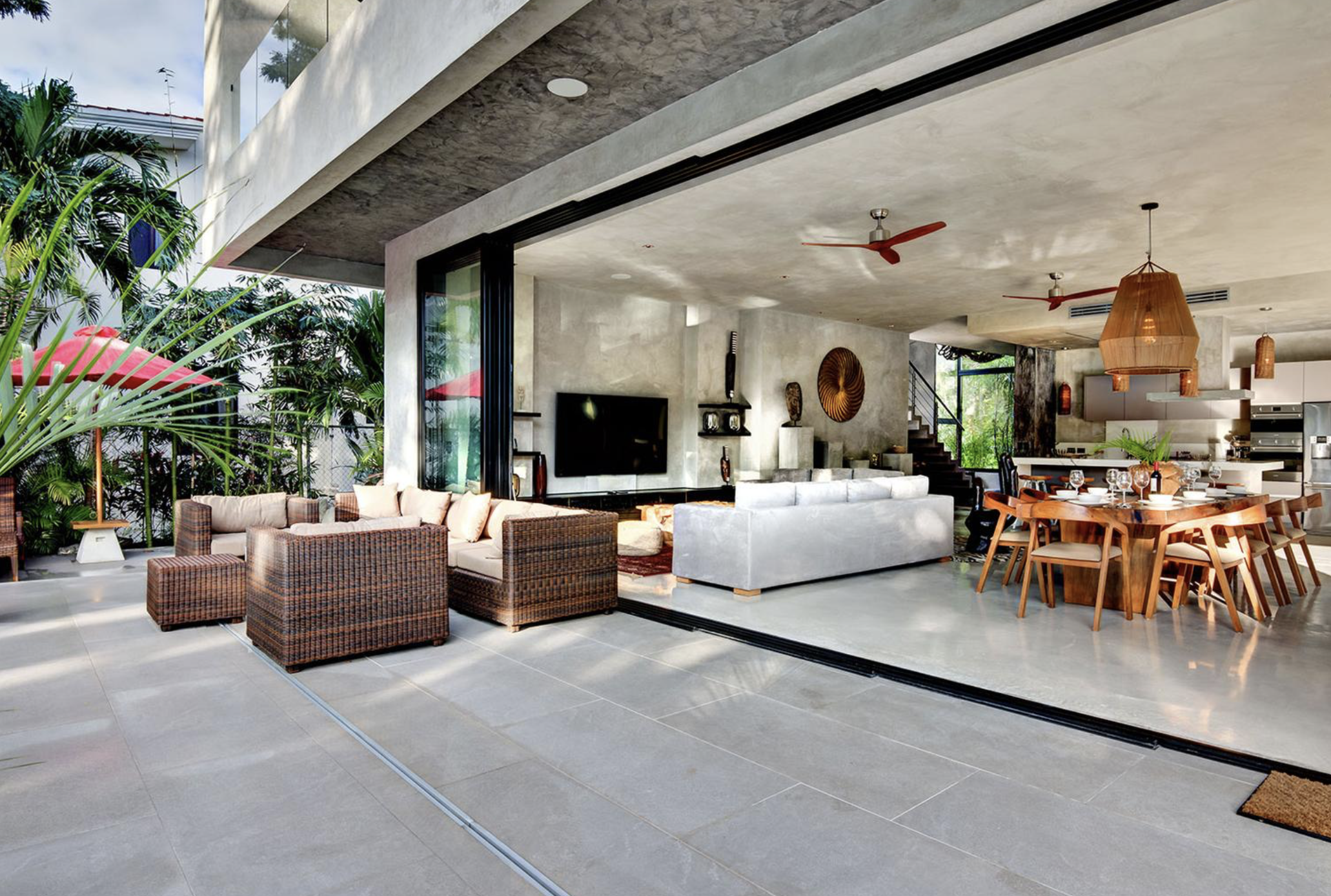 Interior y terraza de una casa moderna con muebles de madera y piedra, decoración en tonos neutros, áreas de comedor y sala, con plantas y ventanas grandes que dejan entrar luz natural.