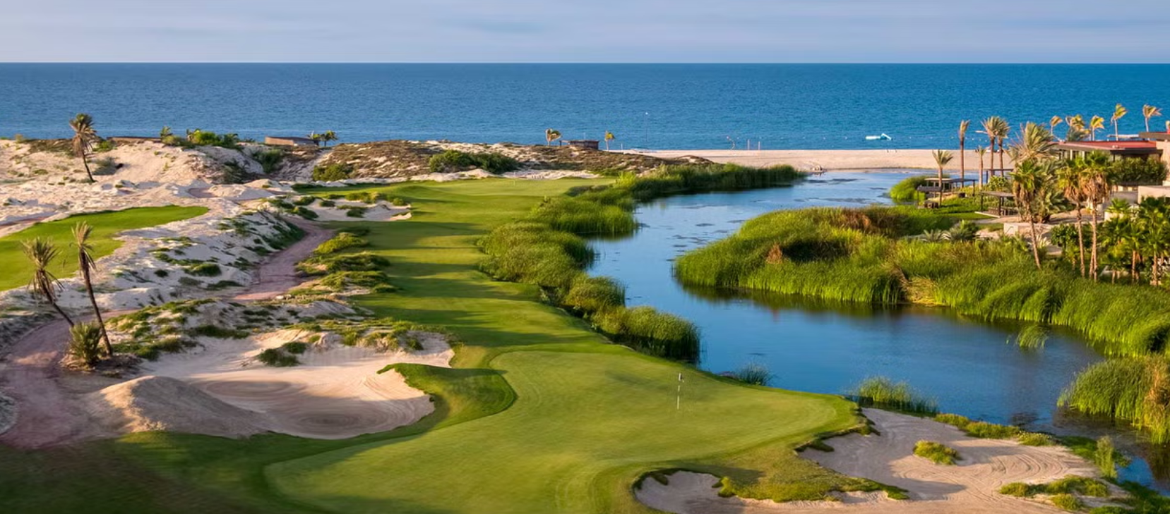 Campo de golf junto a la playa con áreas verdes, arboledas y agua, y el mar al fondo.