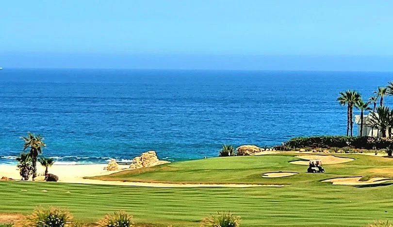 Campo de golf con áreas verdes, arena y palmeras junto al mar