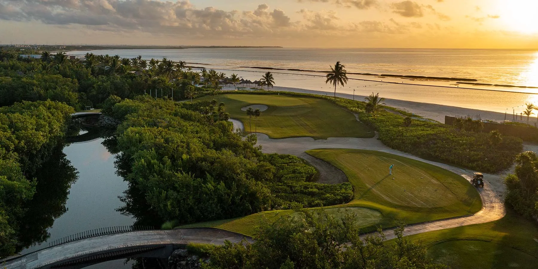 Paisaje de un campo de golf junto a la playa con palmeras, lago y camino en un atardecer