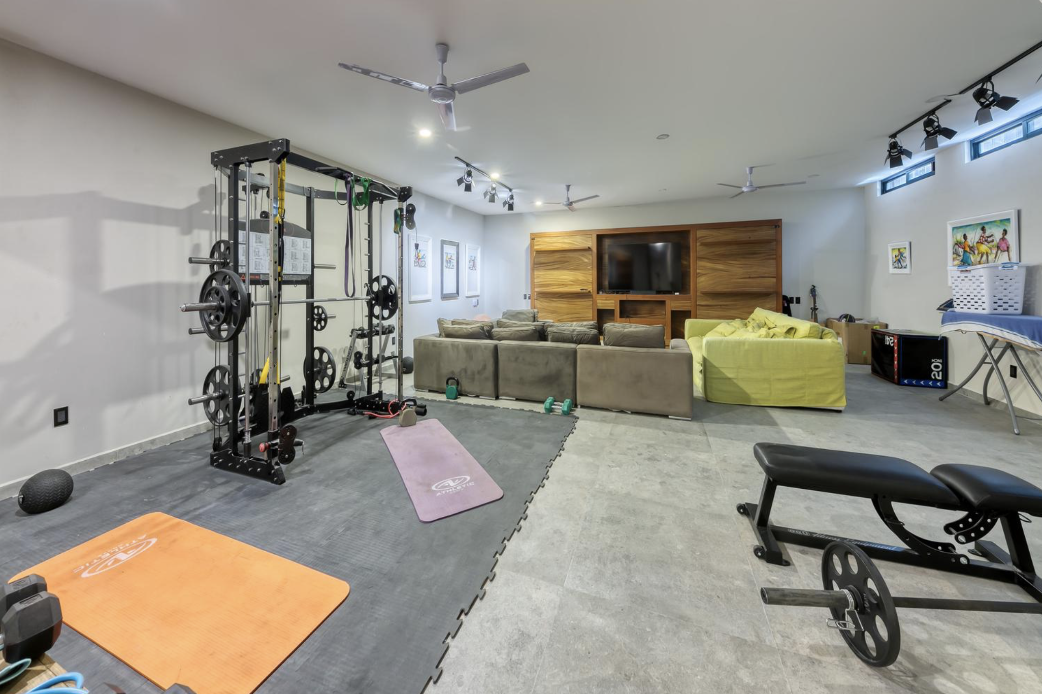 Sala de gimnasio y área de entretenimiento con sillones, televisión y equipo de ejercicio.