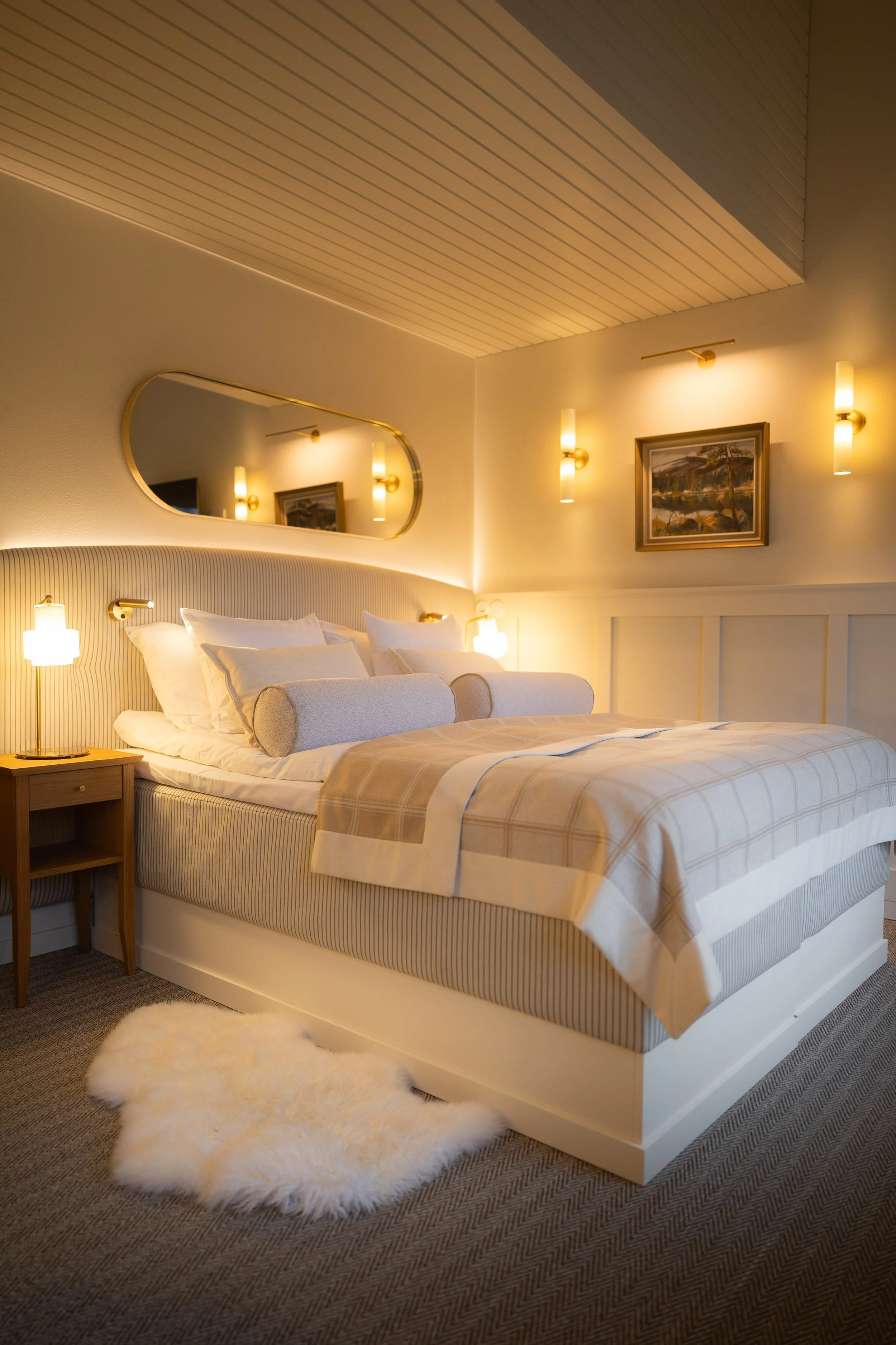 Habitación de hotel con cama grande, almohadas, una alfombra de pelo y lámparas de pared