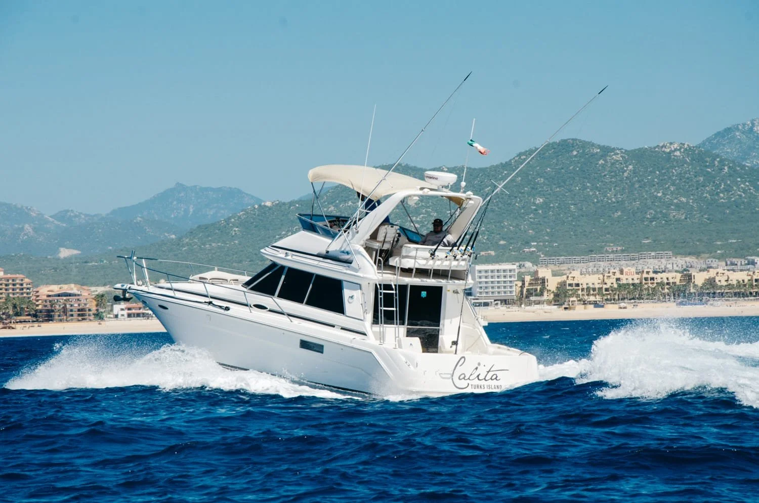 Yate blanco navegando en mar con costas y montañas al fondo.