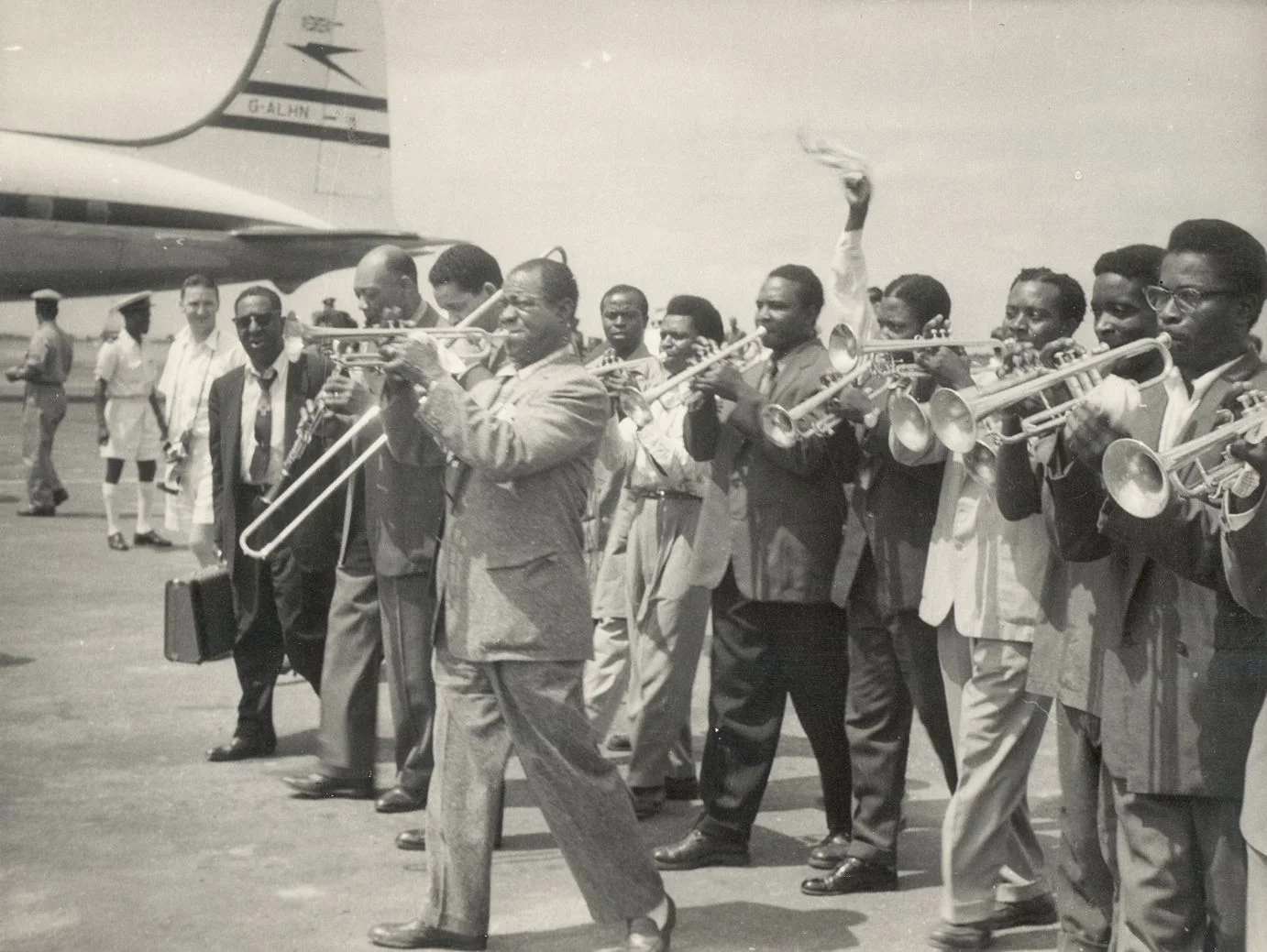 Louis Armstrong (center) is greeted by nine local trumpet players at the airport in Accra, The Gold Coast (present day Ghana) in 1956. Credit: Courtesy of the Louis Armstrong House Museum
