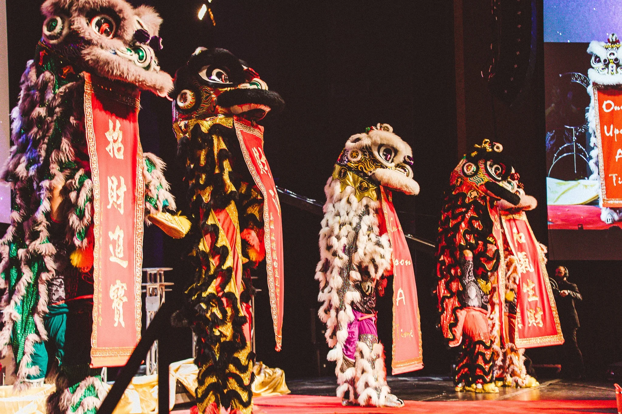 Lion dance performers on stage wearing colorful costumes and lion masks during a cultural celebration.