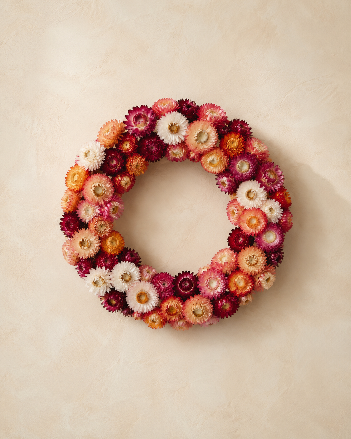A decorative flower wreath made of colorful flowers in shades of pink, red, white, and orange, placed on a cream-colored surface.