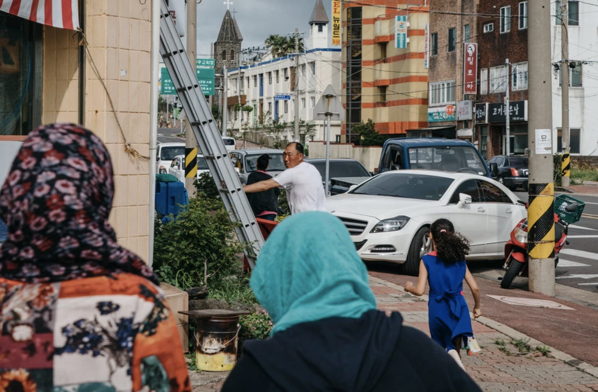 A Korean man turns his head towards two Yemeni refugee women on the streets of a town on Jeju Island. Credit: Jun Michael Park/ The New York Times