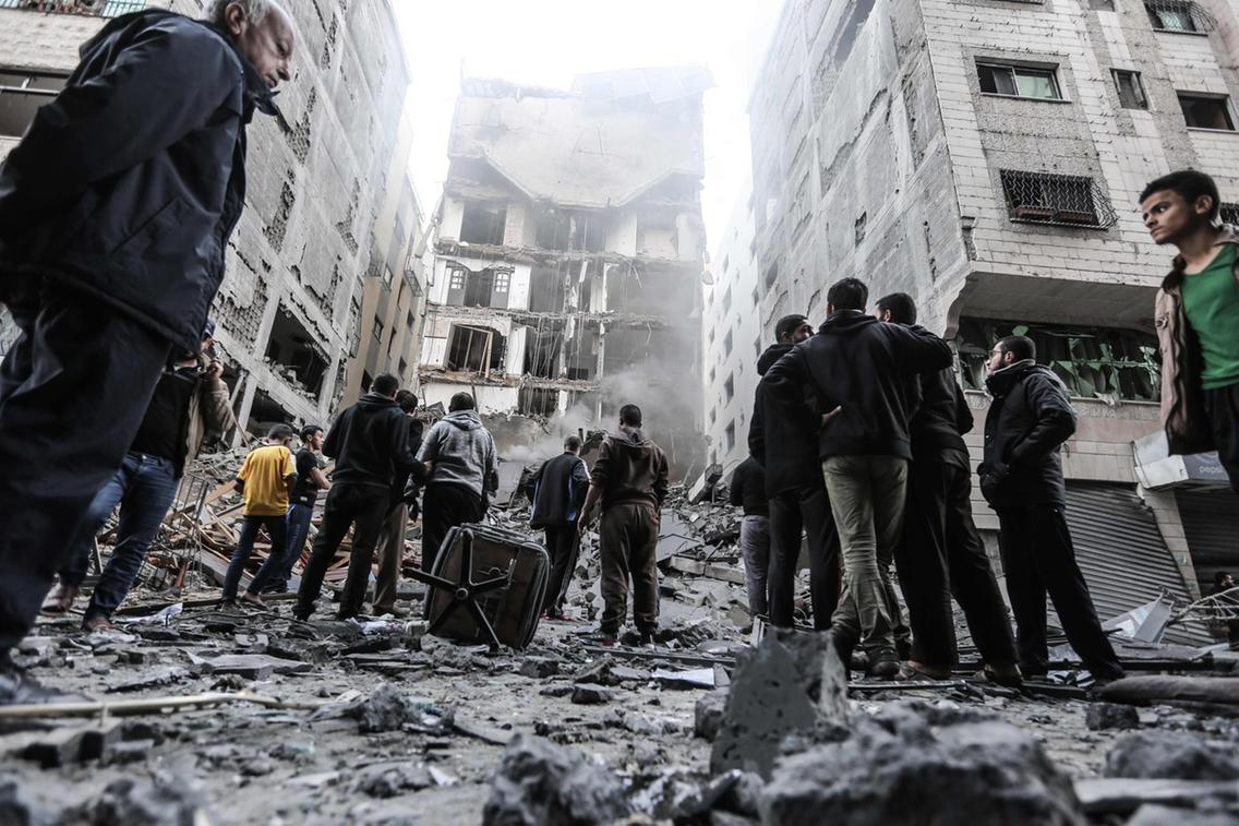 Palestinians gather in front of damaged buildings in Gaza City following Israeli air strikes. Credits: AFP