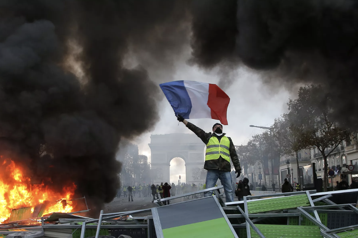 Protestors wearing yellow vests wave the French flag along the Champs Elysées. Source: Michel Euler/AP