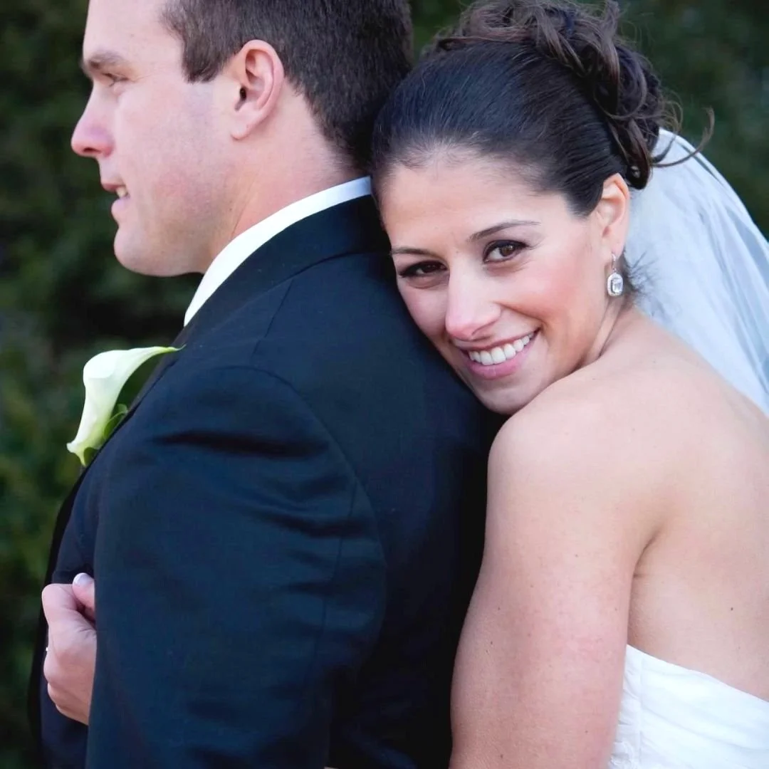 CT makeup on a smiling bride leaning on a groom's back during wedding photos.