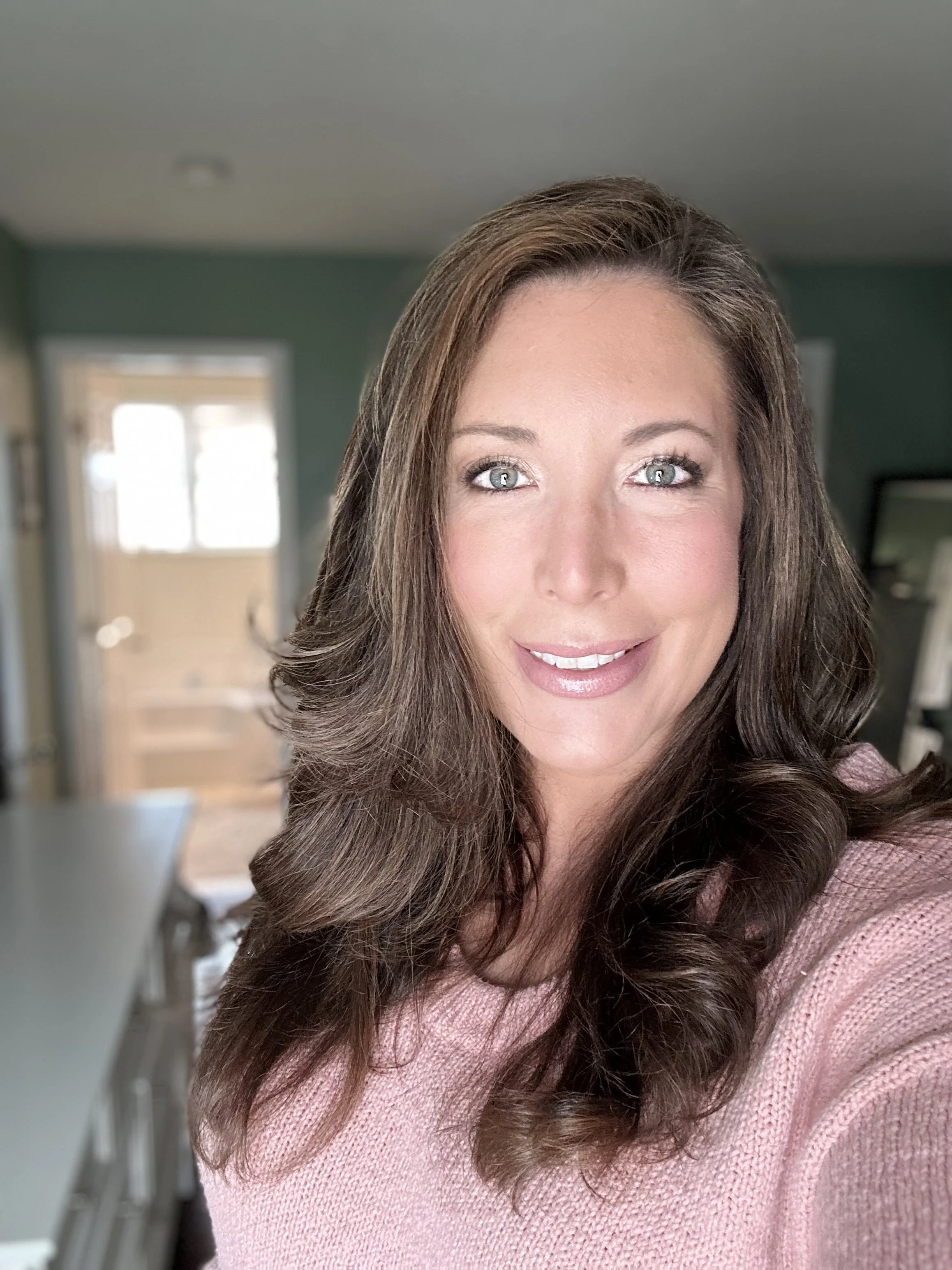 A CT Makeup Artist teaching makeup lessons with long, dark brown hair and blue eyes, smiling in a close-up portrait against a neutral background.
