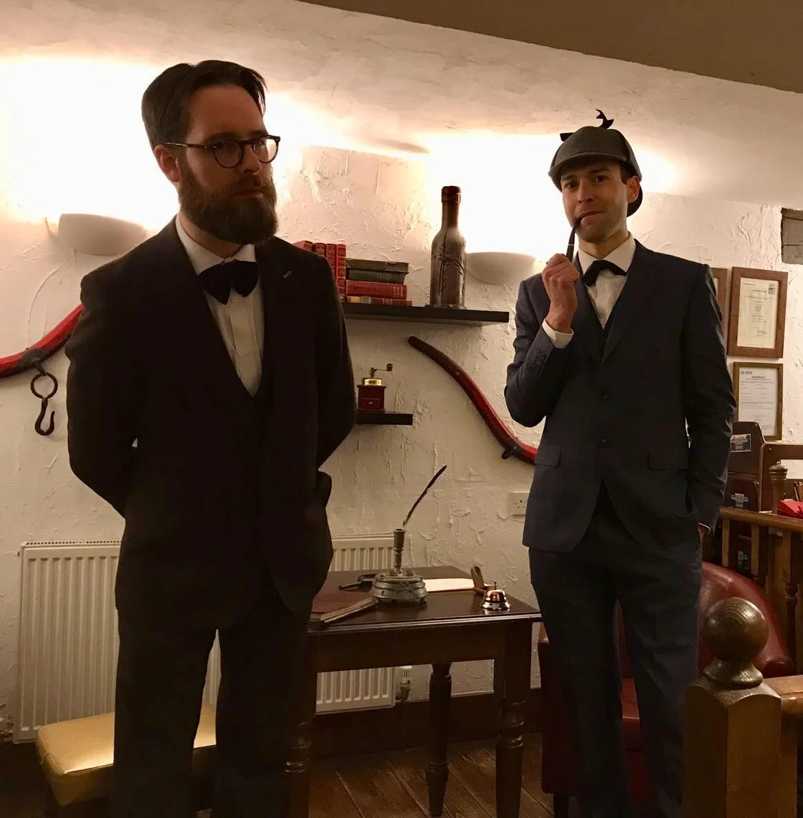 Holmes looks on, amused, as Watson regards the audience suspiciously. 